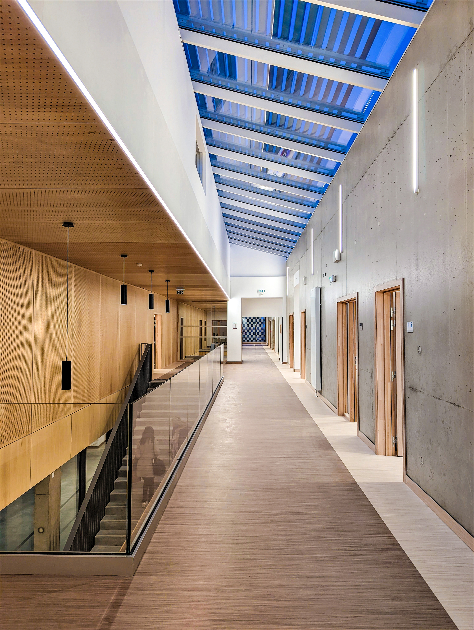 Upper-level corridor with glazed balustrade overlooking lower floor beneath a slatted skylight