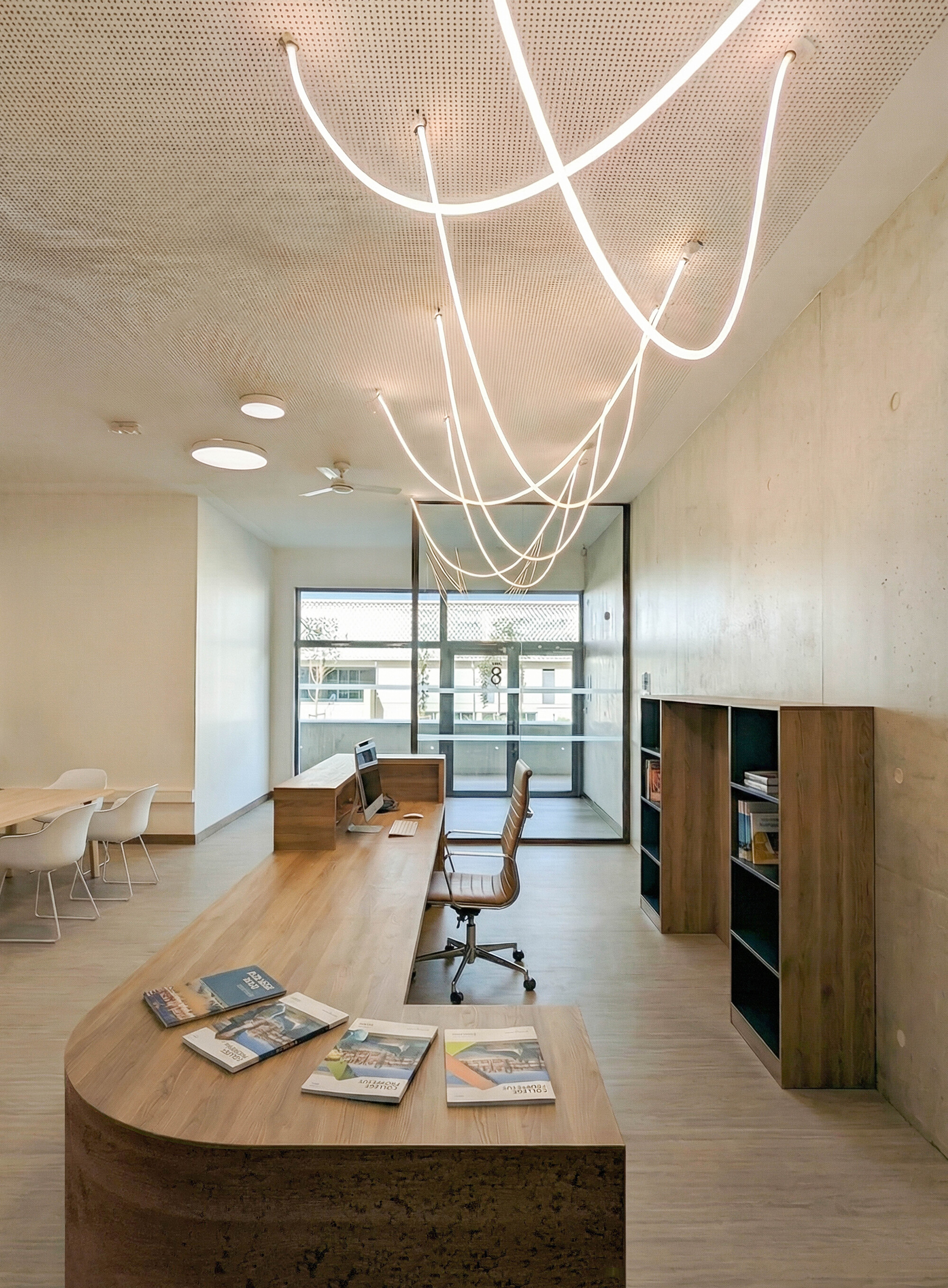 Curved white neon light installation hanging above a timber desk with magazines in the reading area