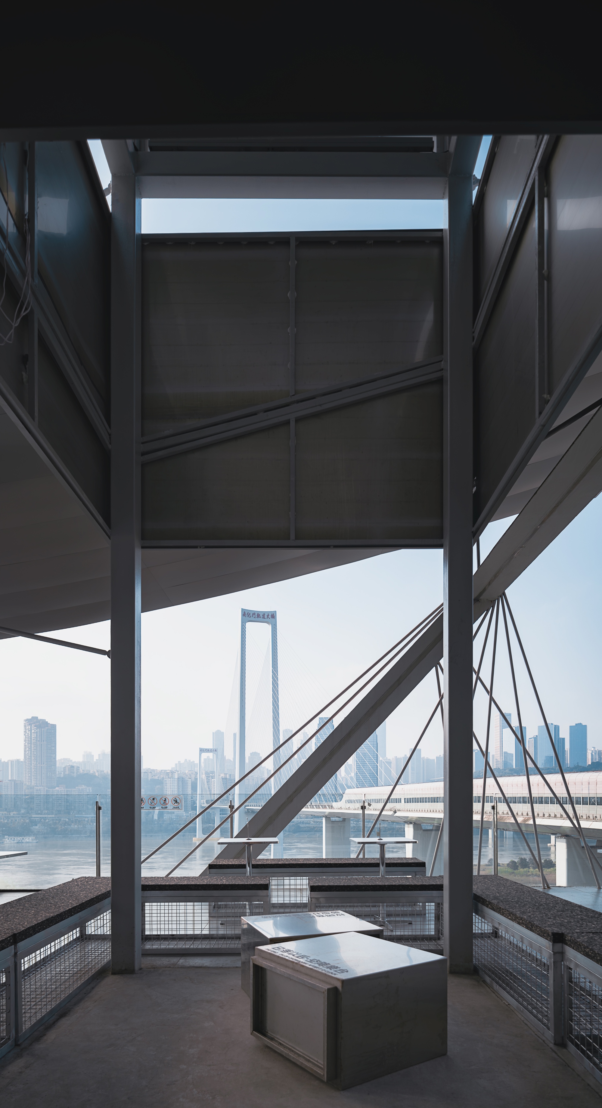 View through steel structural bracing toward a waterfront bridge under a misty sky