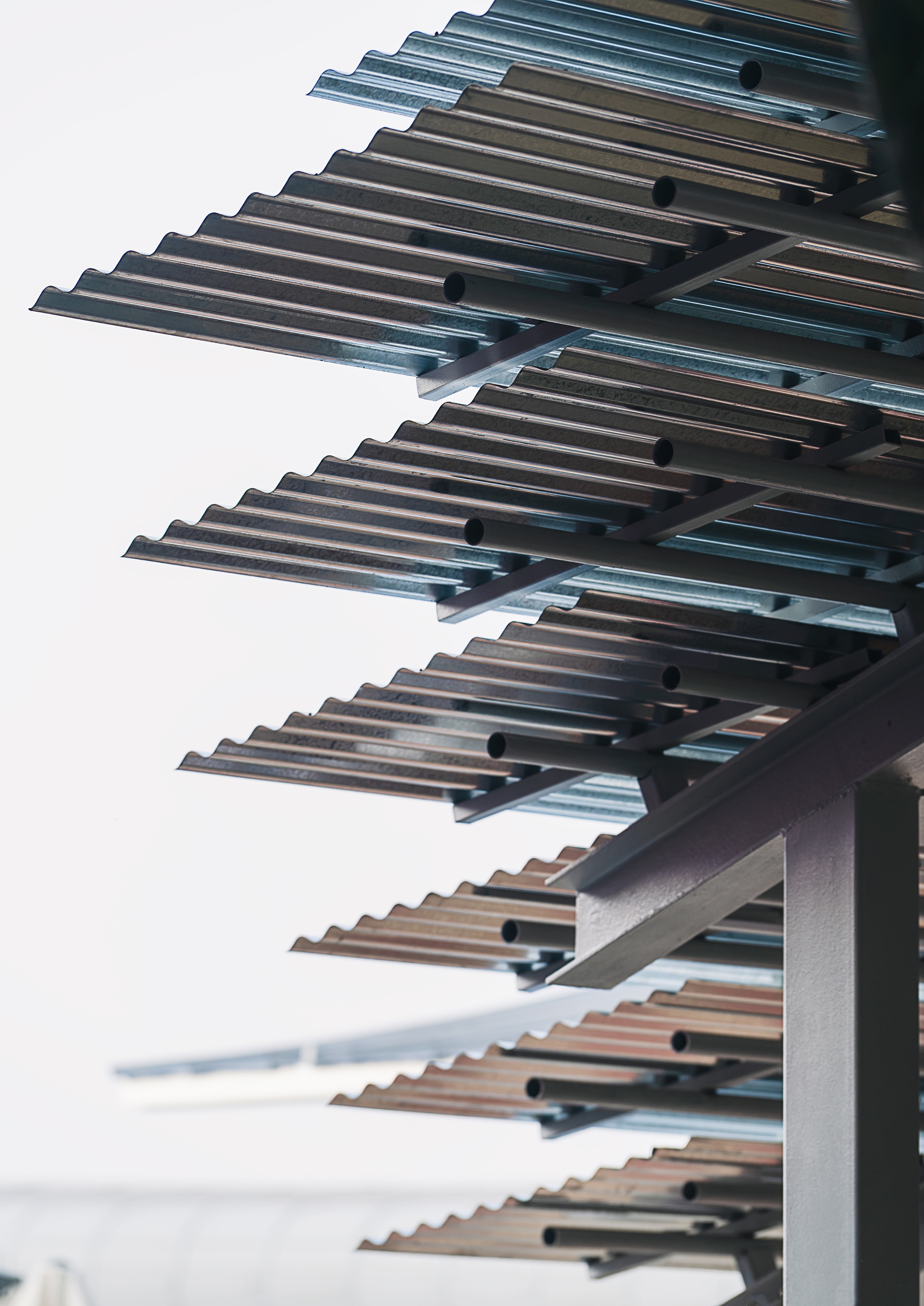 Upward view of cantilevered metal louvres extending from a white facade against an overcast sky