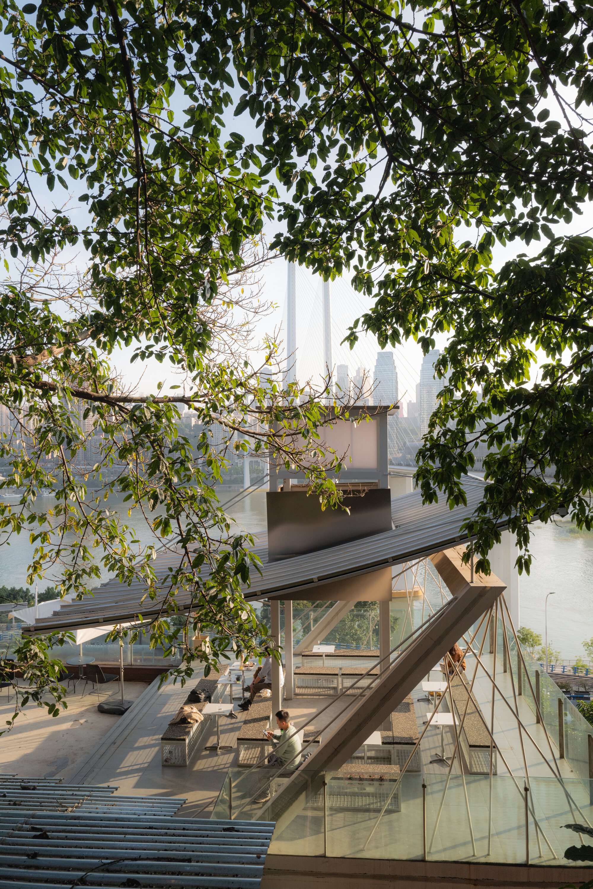 View through tree branches of an open timber pavilion with glass balustrade in morning haze