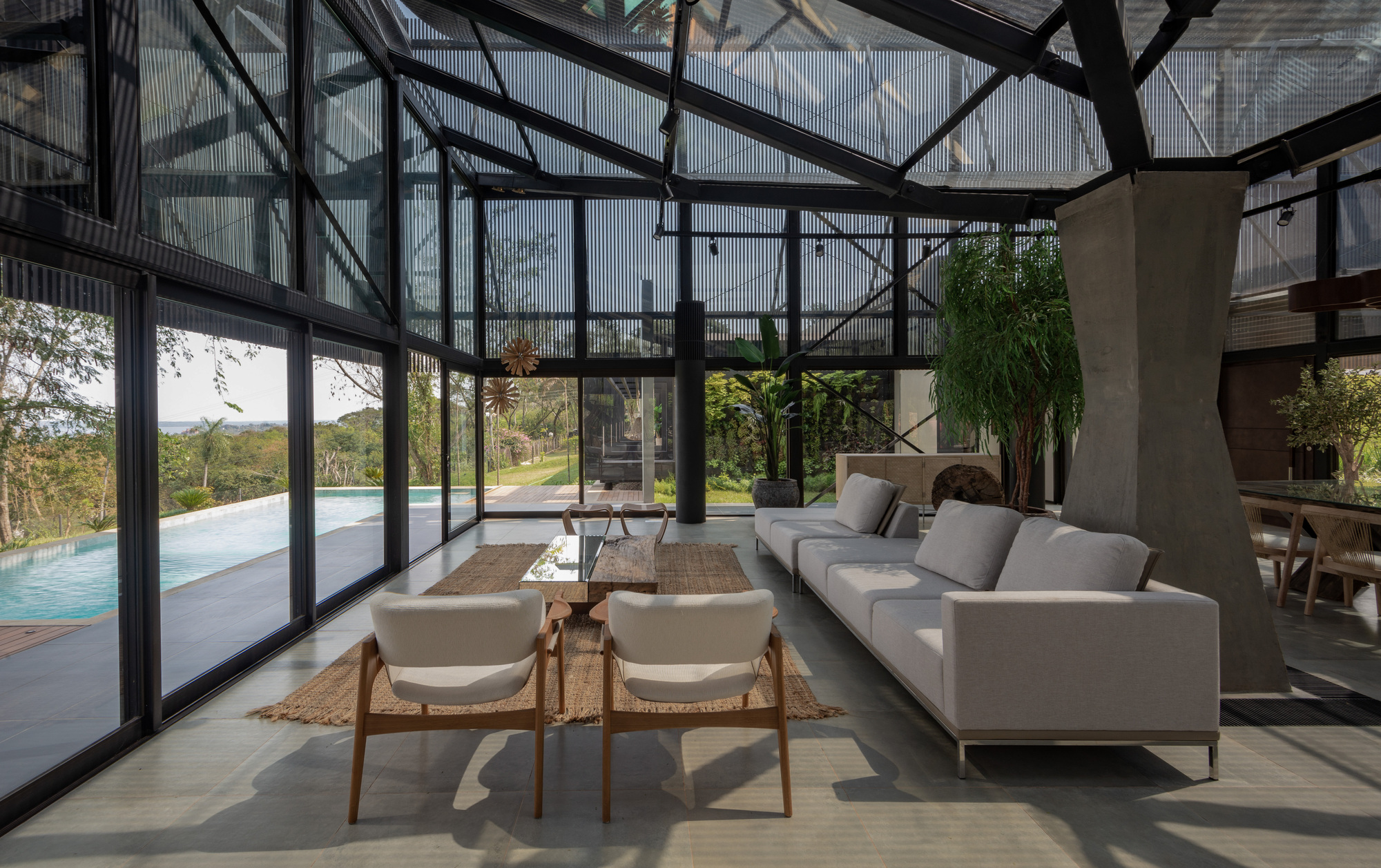 Glass-walled living room with exposed steel trusses overhead and a pool terrace visible beyond