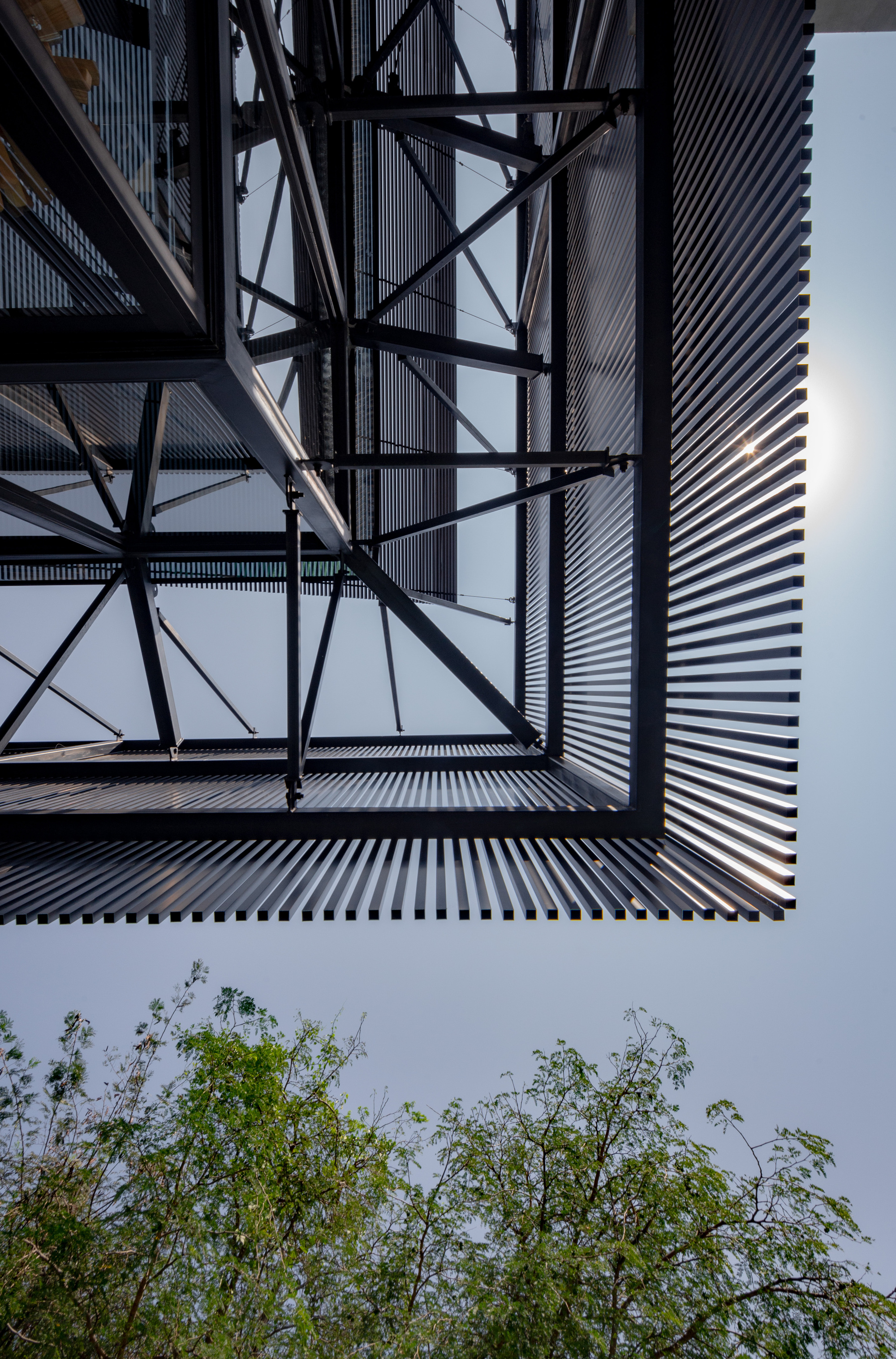 Upward view of the diagonal steel bracing and corrugated facade with treetops visible below