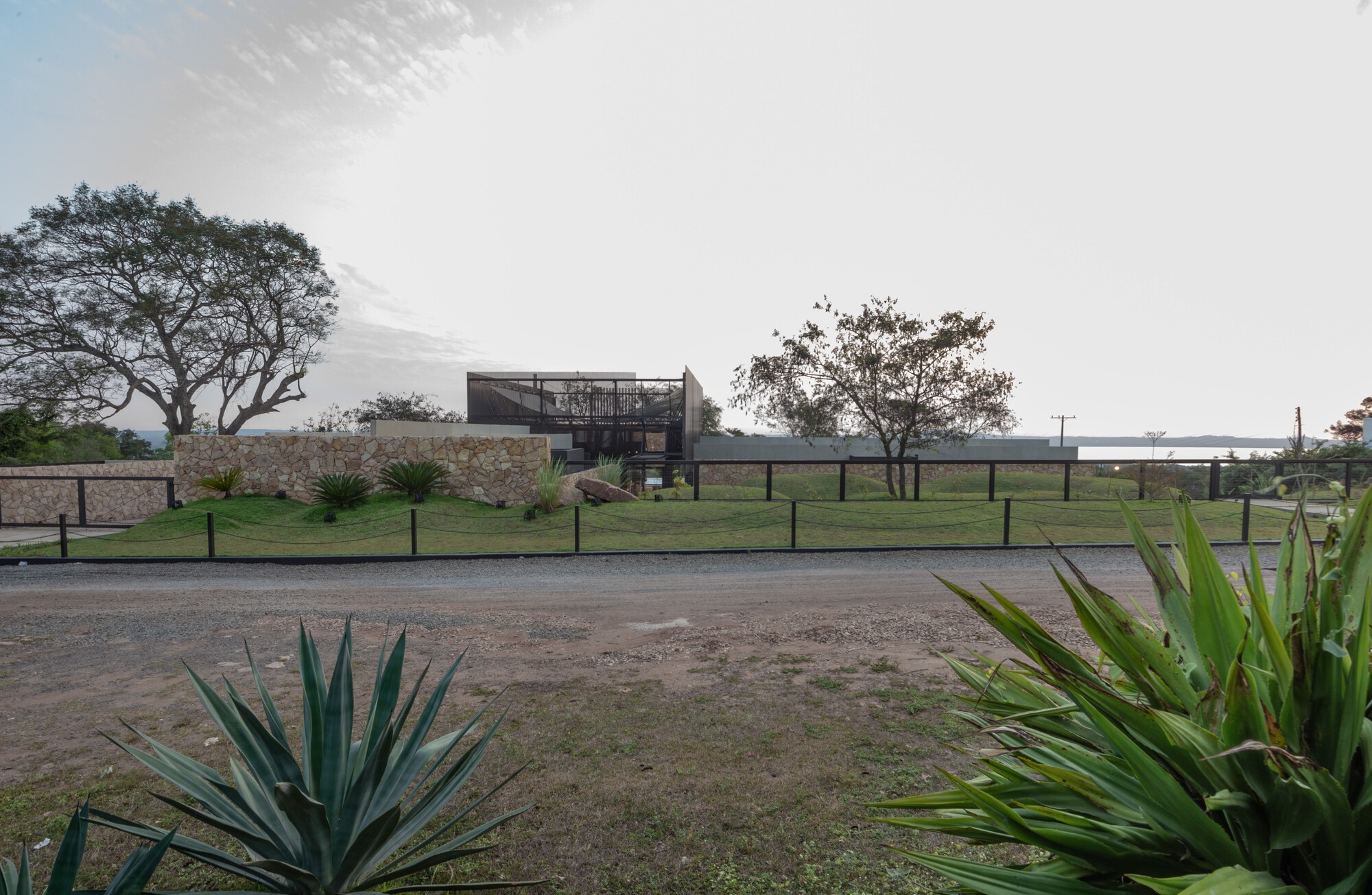 Distant view of the elevated steel and screen volume above a stone retaining wall at dusk