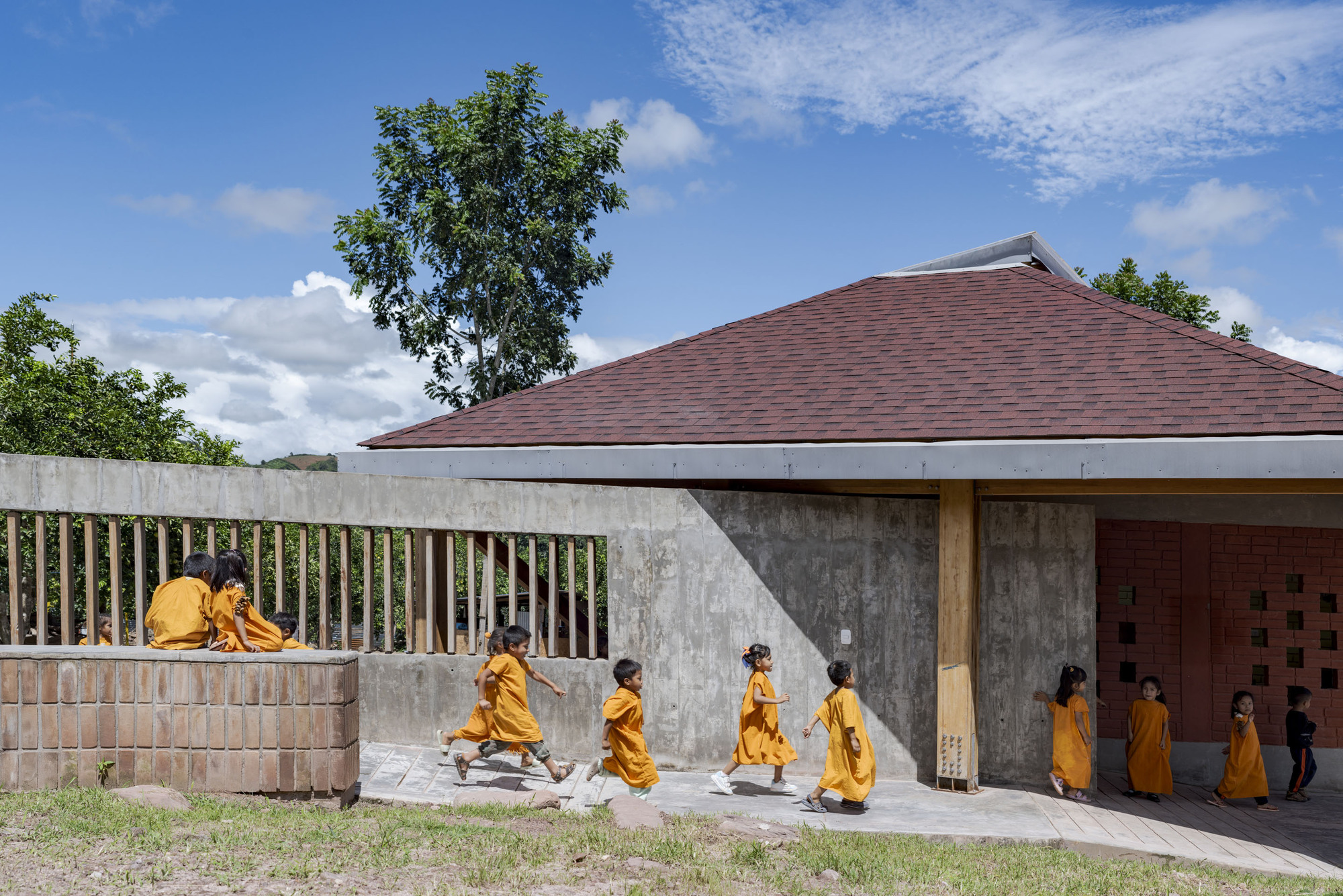Concrete boundary wall with vertical timber slats and raised seating ledge where two figures sit under scattered clouds