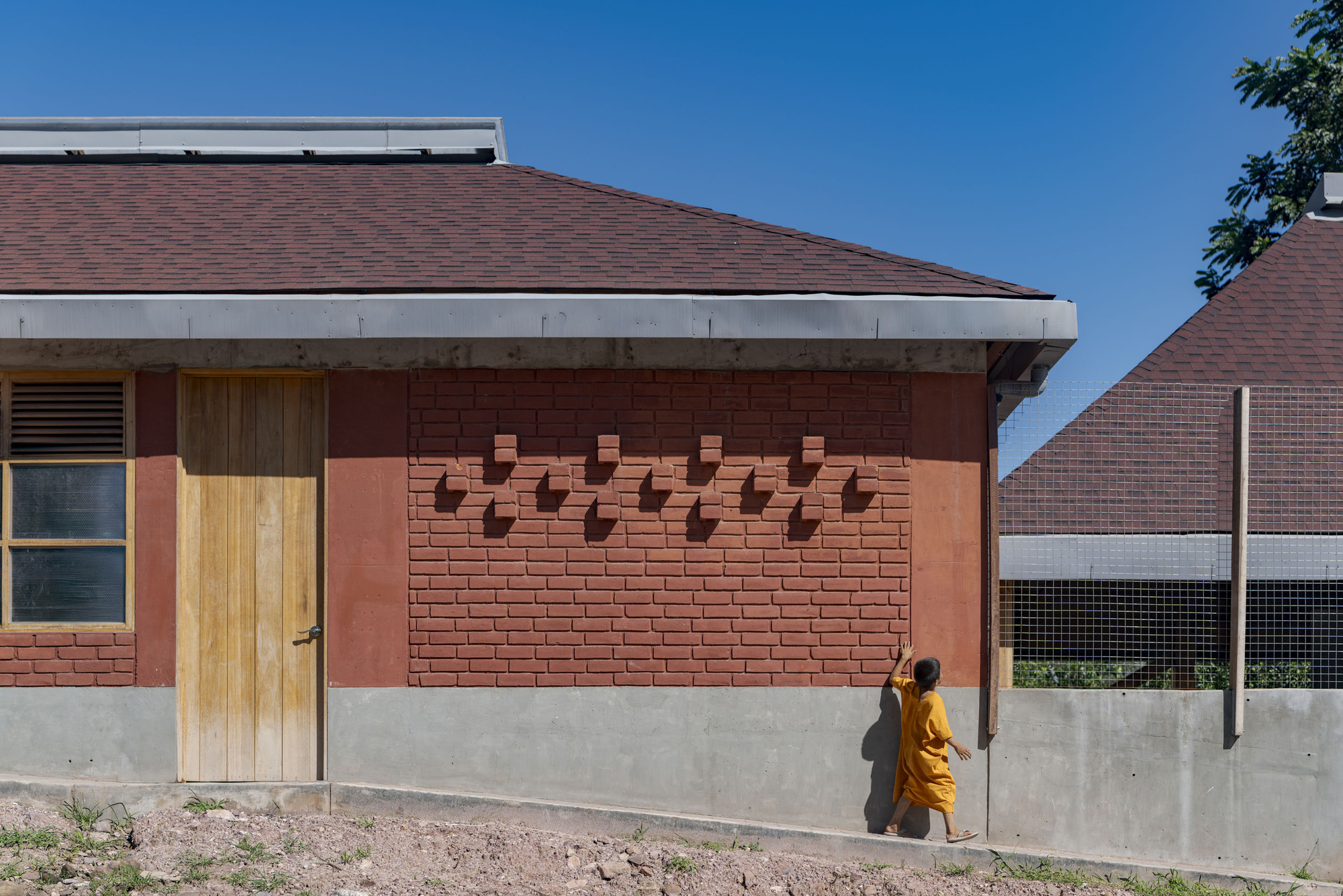 Red brick facade with protruding brick patterns and timber door set above a smooth concrete base wall