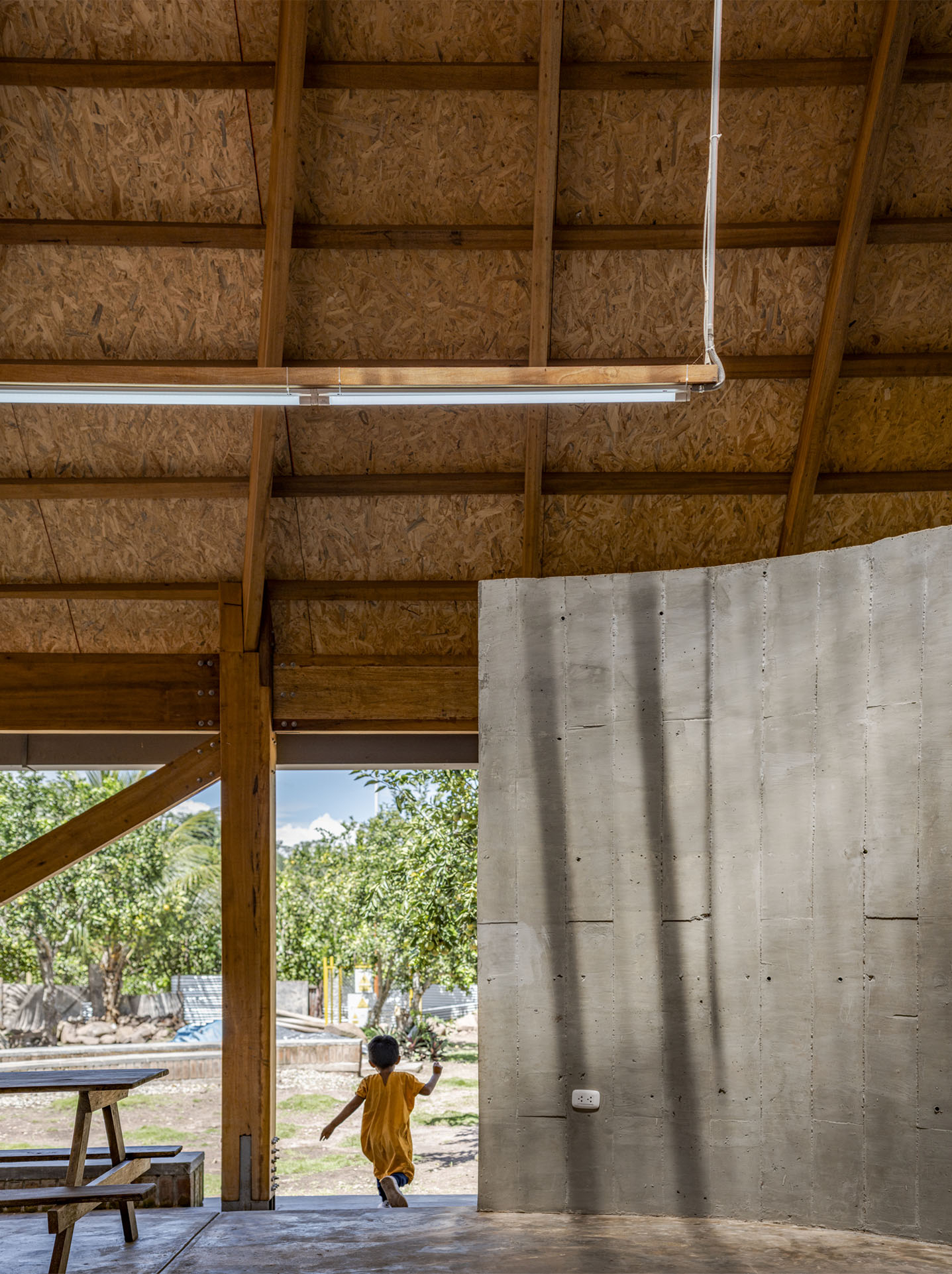 Timber-framed ceiling with exposed beams and fluorescent lighting tube above a board-formed concrete wall