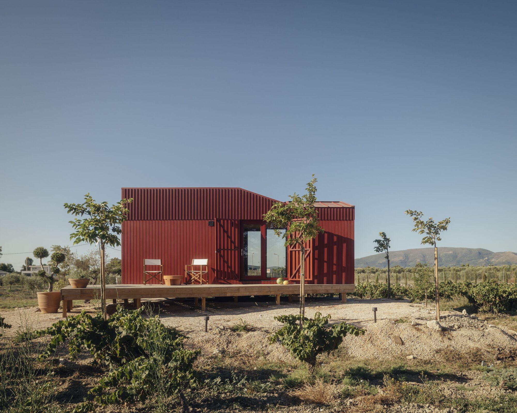 Red corrugated metal pavilion with covered deck and planted terrace in a dry landscape