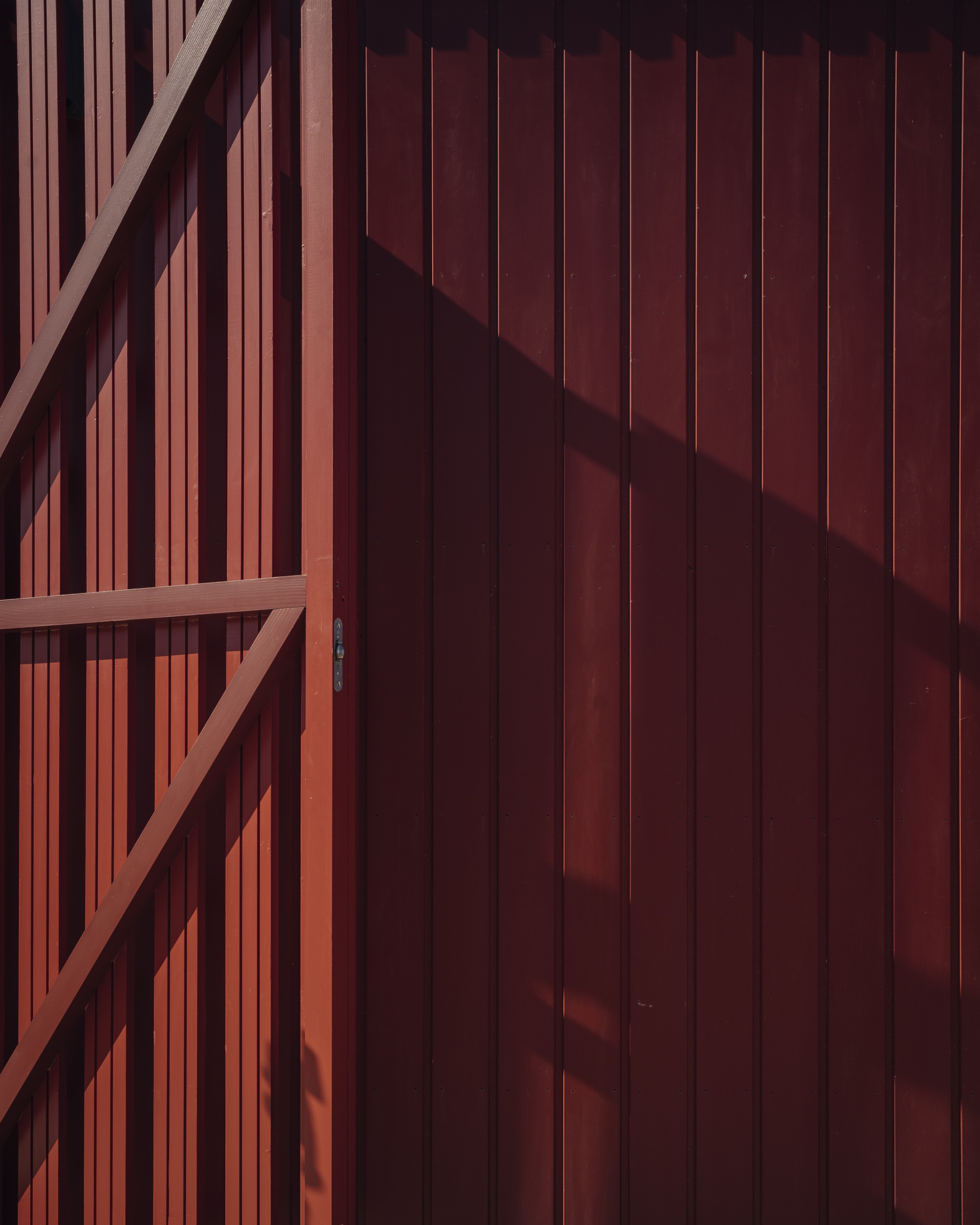 Timber-framed sliding door with vertical battens casting angular shadows across the red-stained wood cladding
