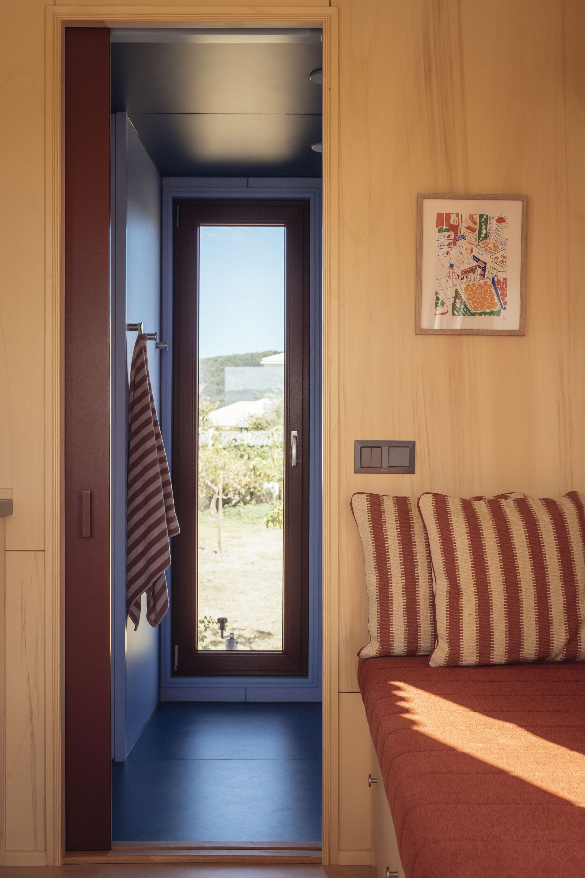 View through plywood-lined doorway to a narrow bathroom with glazed door framing coastal landscape beyond