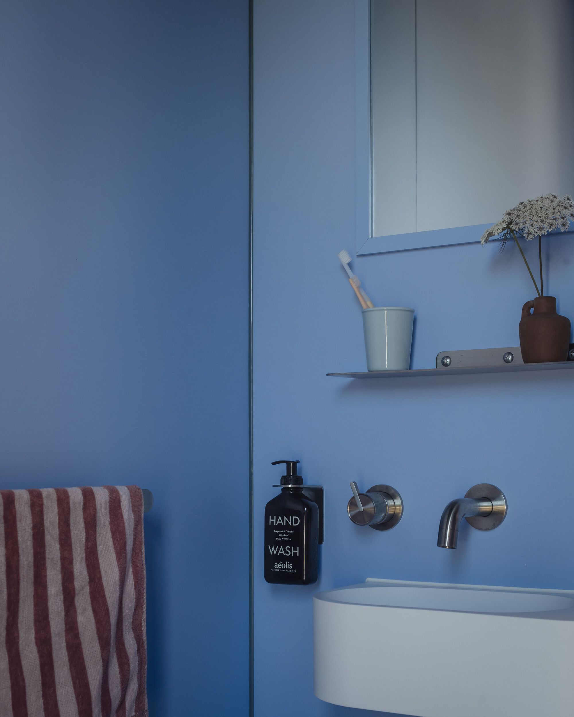 Wall-mounted basin with circular chrome taps and shelf against powder blue tiled surfaces