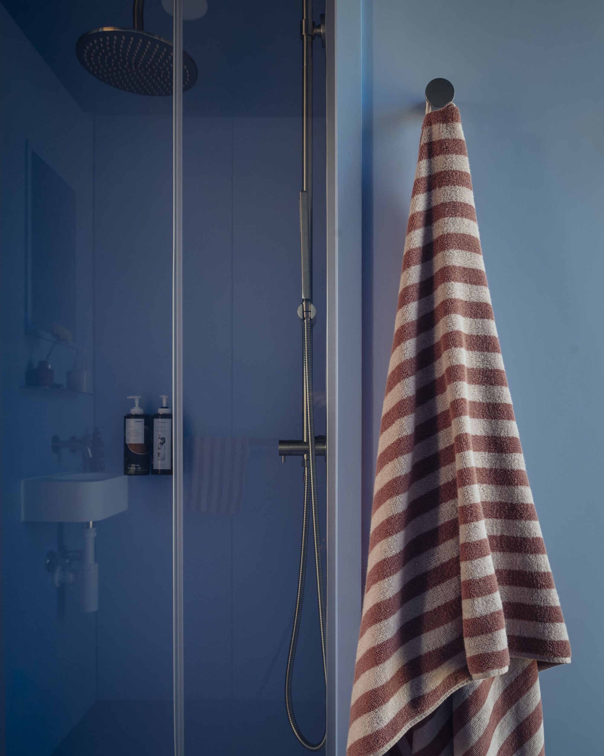 Glass shower enclosure with overhead rain head and striped towel hanging on blue wall