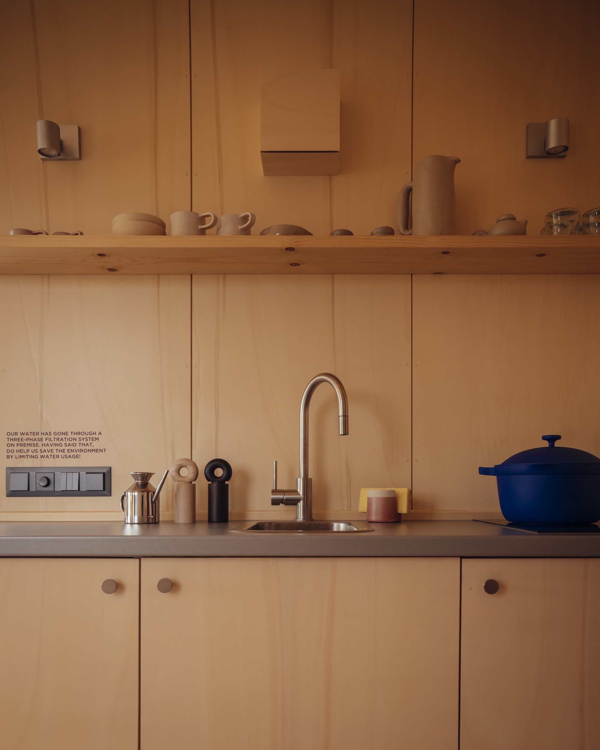 Kitchen counter with timber paneling, open shelf displaying ceramics, and gooseneck faucet at sink