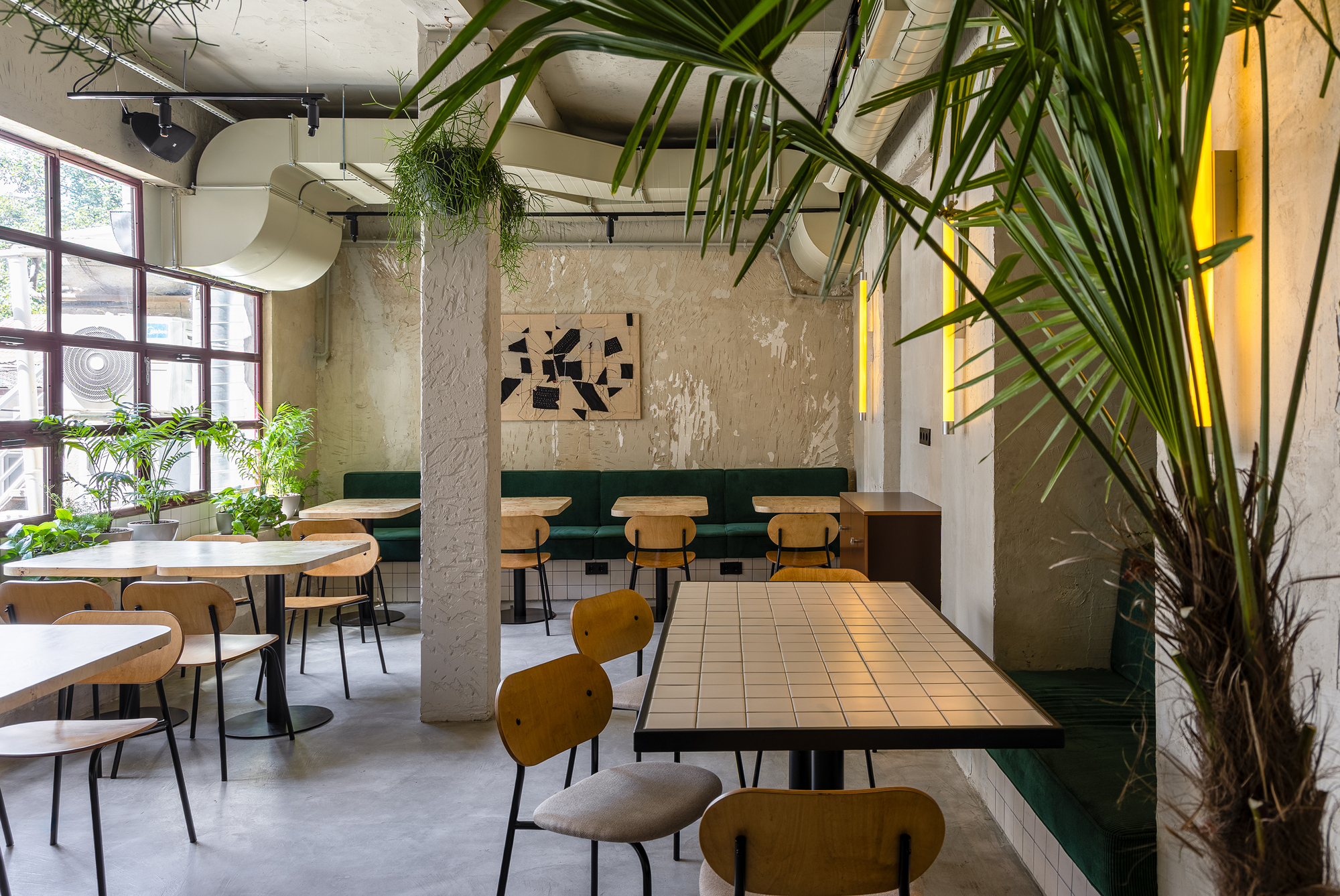 Dining area with exposed concrete ceiling, large palms, weathered plaster walls and tile-topped tables under natural light