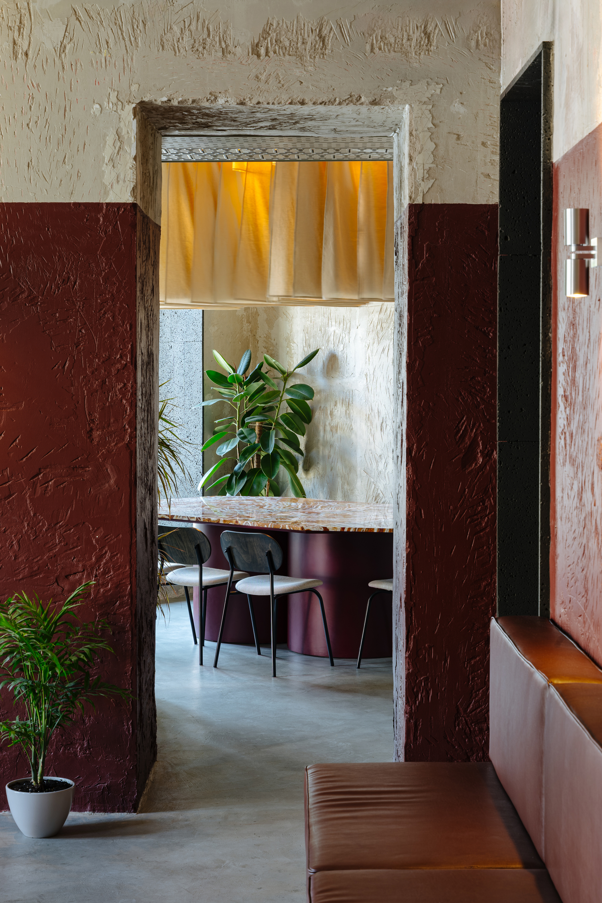Doorway framed by maroon plaster walls revealing dining space with yellow curtain above and potted greenery