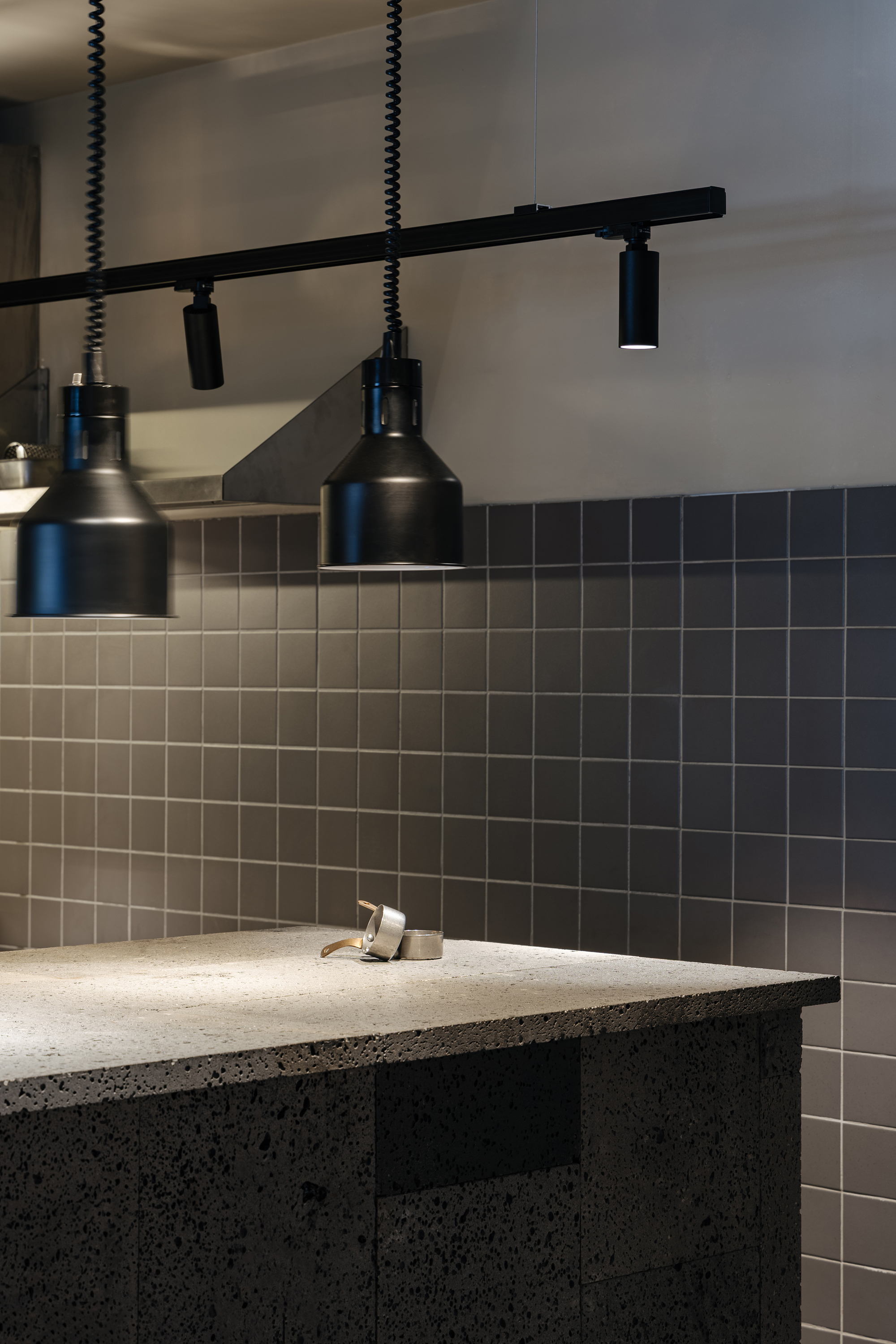 Bathroom sink with dark mosaic tile backsplash and black pendant track lighting above