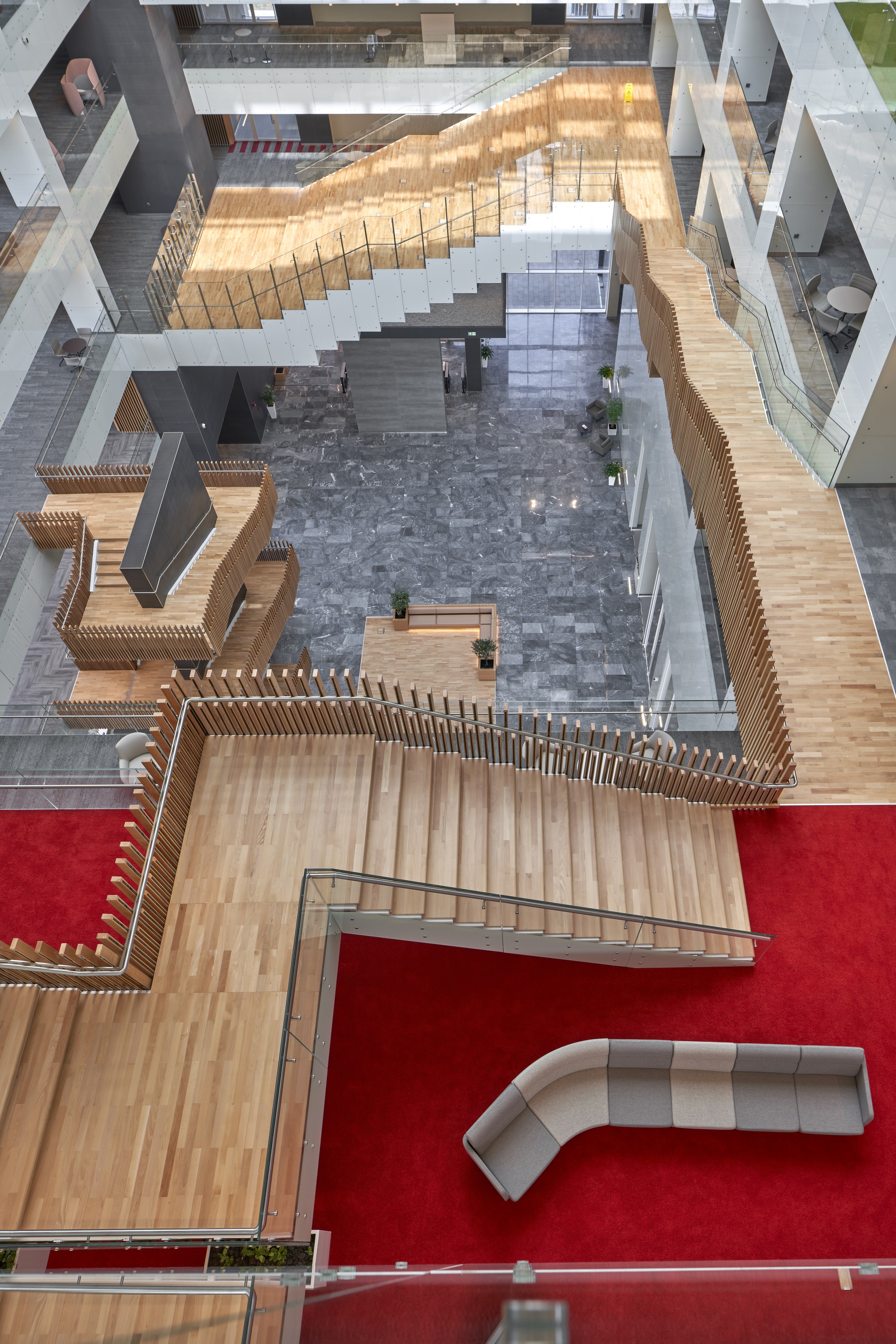 Top-down view of the atrium showing timber slatted balustrades wrapping stair flights and red carpet zones