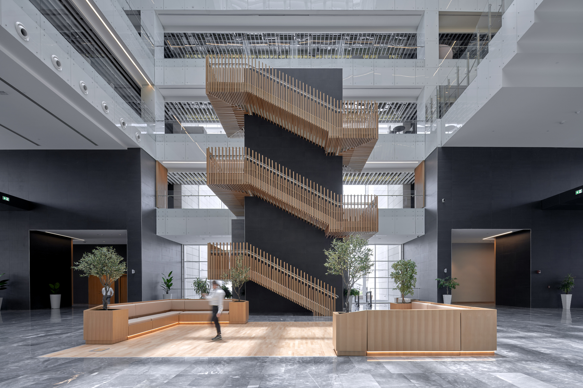 Ground-level lobby with timber-clad monumental stair cascading through the atrium and planters with trees
