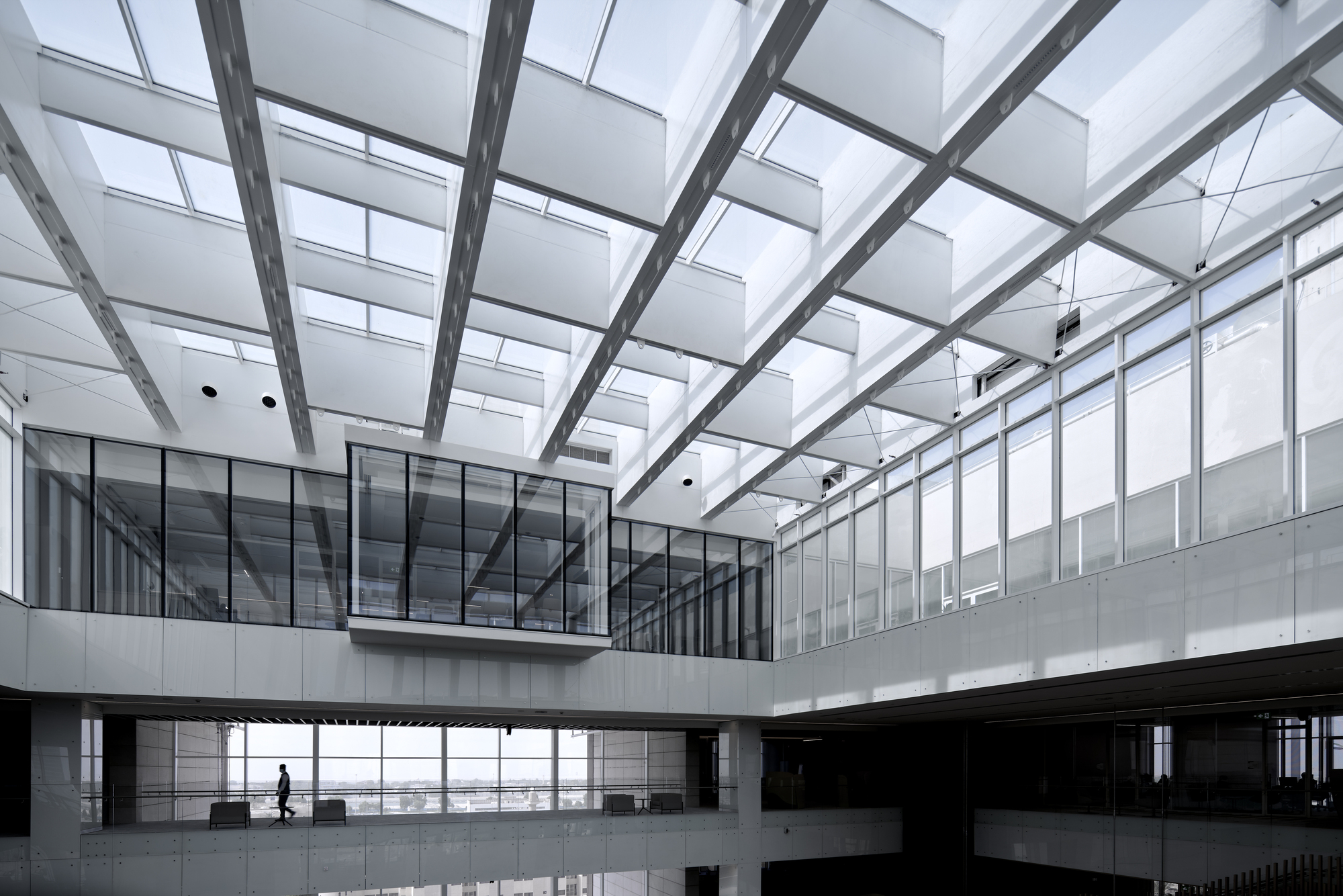 Interior courtyard beneath structural grid skylight with person walking along upper-level bridge