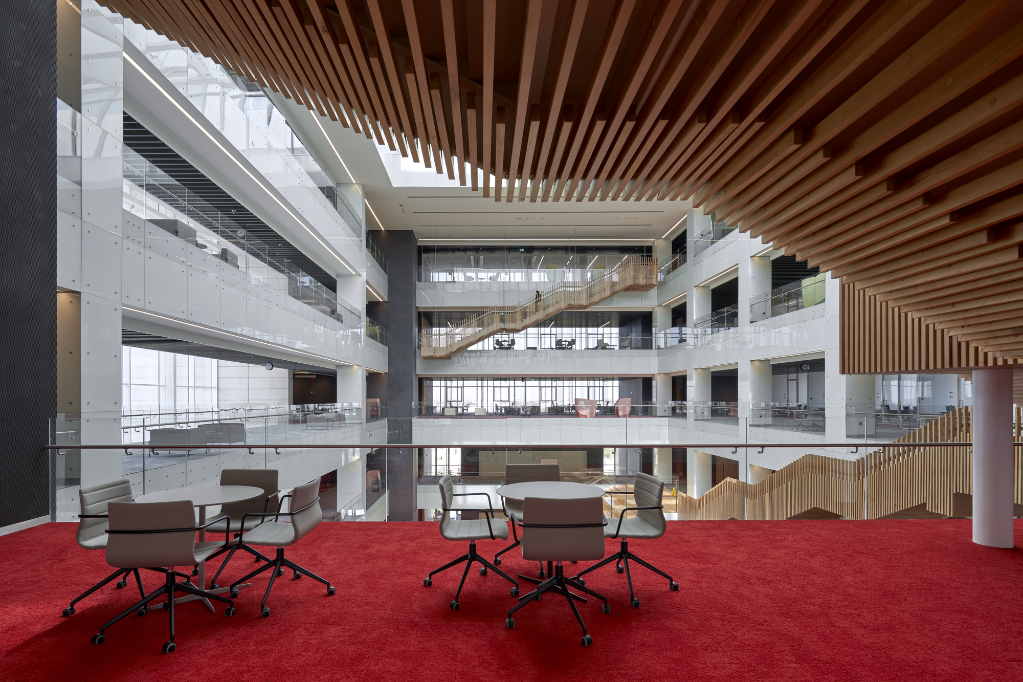 Atrium level with red carpeted floor and slatted timber ceiling above scattered work tables