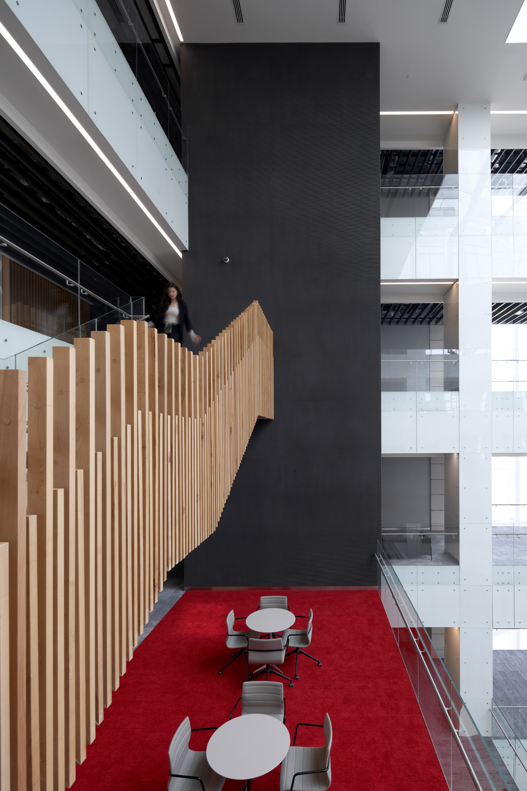 Tall black column beside curving timber-slatted stair balustrade with figure ascending in motion blur