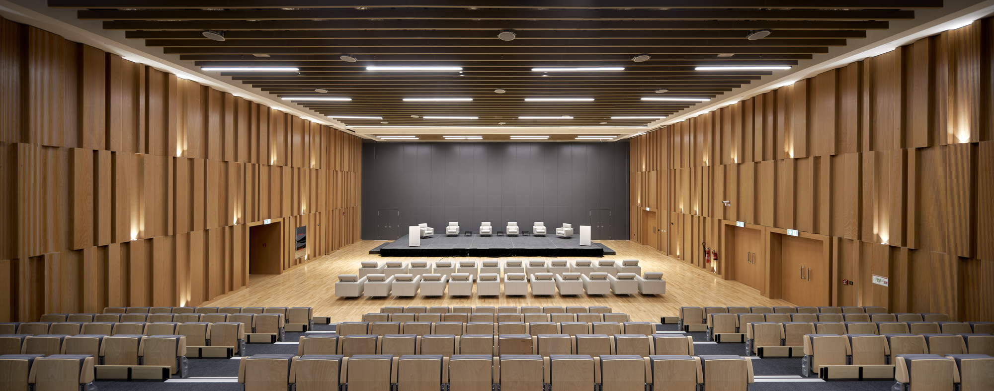 Auditorium with tiered seating facing dark grey stage wall beneath articulated timber side panels