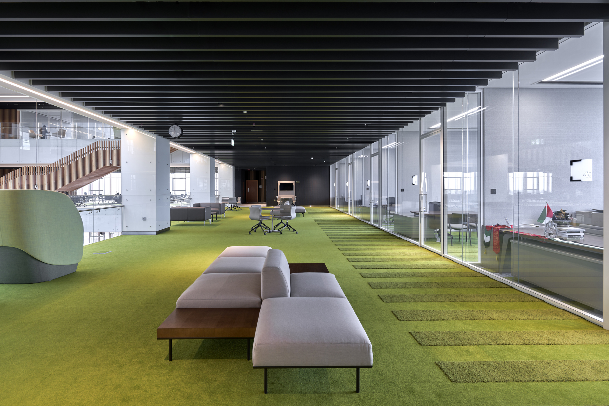 Interior corridor with graduated yellow and green carpet tiles running beneath a black slatted ceiling