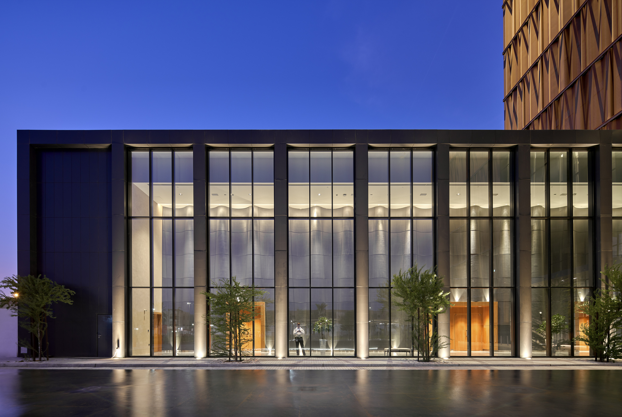 Glazed entrance facade with tall curtain wall and reflecting pool at dusk with a figure inside