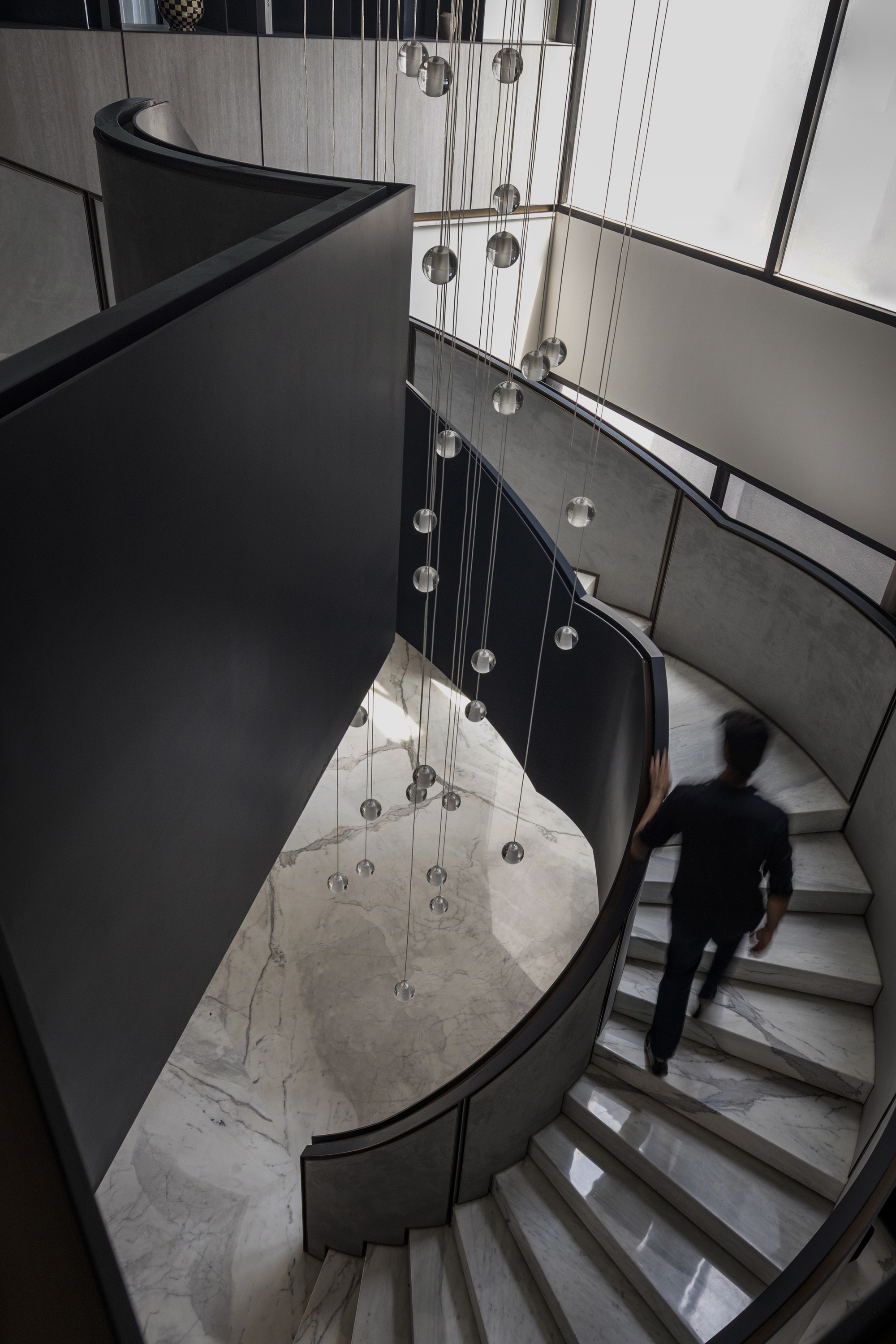 Looking down at curved staircase with marble treads, cluster of globe pendant lights and ascending figure