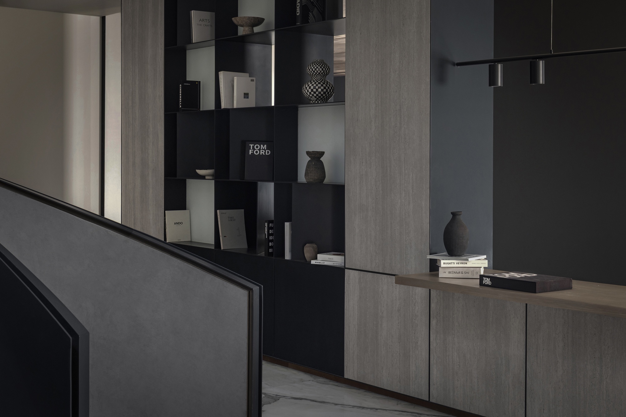 Interior display wall with black recessed shelving holding books and objects beside wood-paneled cabinetry