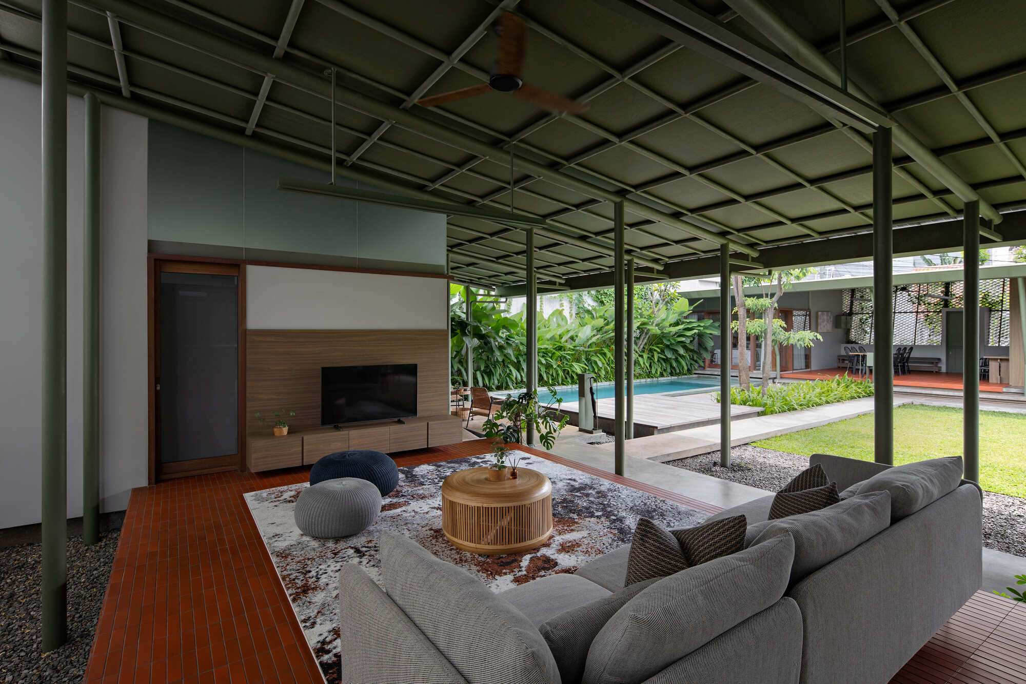 Living area beneath an exposed steel frame ceiling opening to a central lawn and swimming pool
