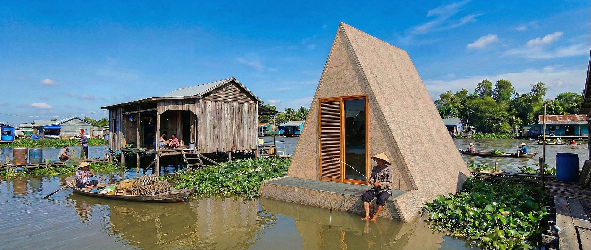 Single triangular shelter on a concrete base floating in a river with boats and stilt houses nearby