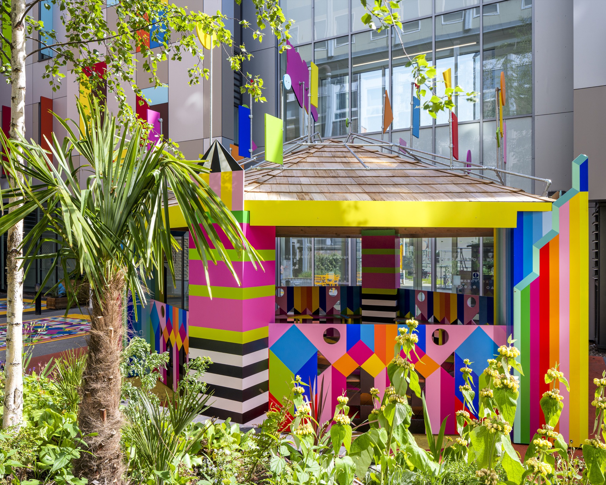 Multicolored pavilion with striped columns and patterned facade surrounded by palm trees and planted beds