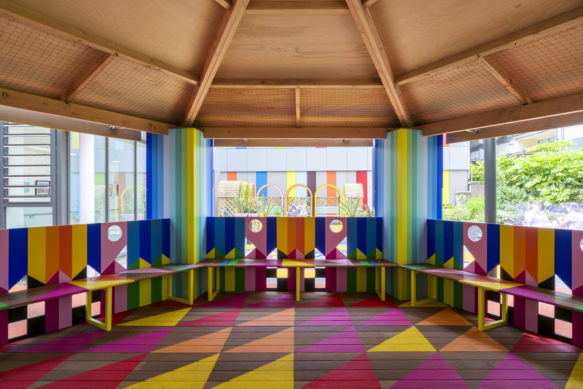 Interior view beneath timber ceiling showing wraparound bench seating with geometric wall panels and floor pattern