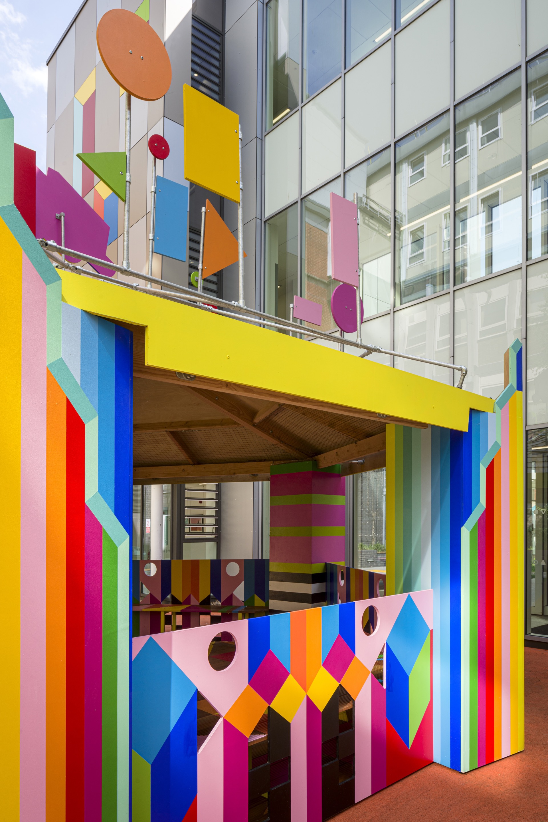 Close view of the pavilion entrance framed by vertical striped columns and geometric shapes on glass and balustrade