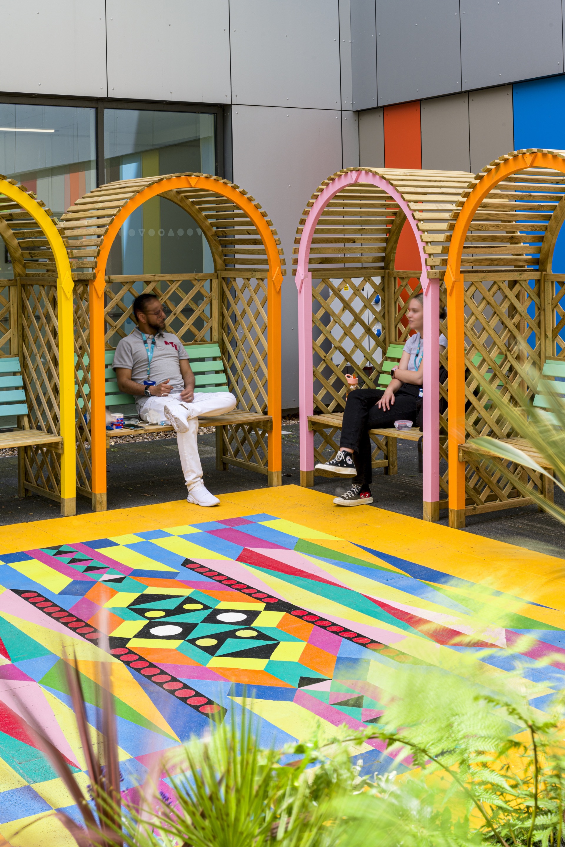 Courtyard with arched timber lattice seating alcoves and multicolored geometric paving beneath planted beds