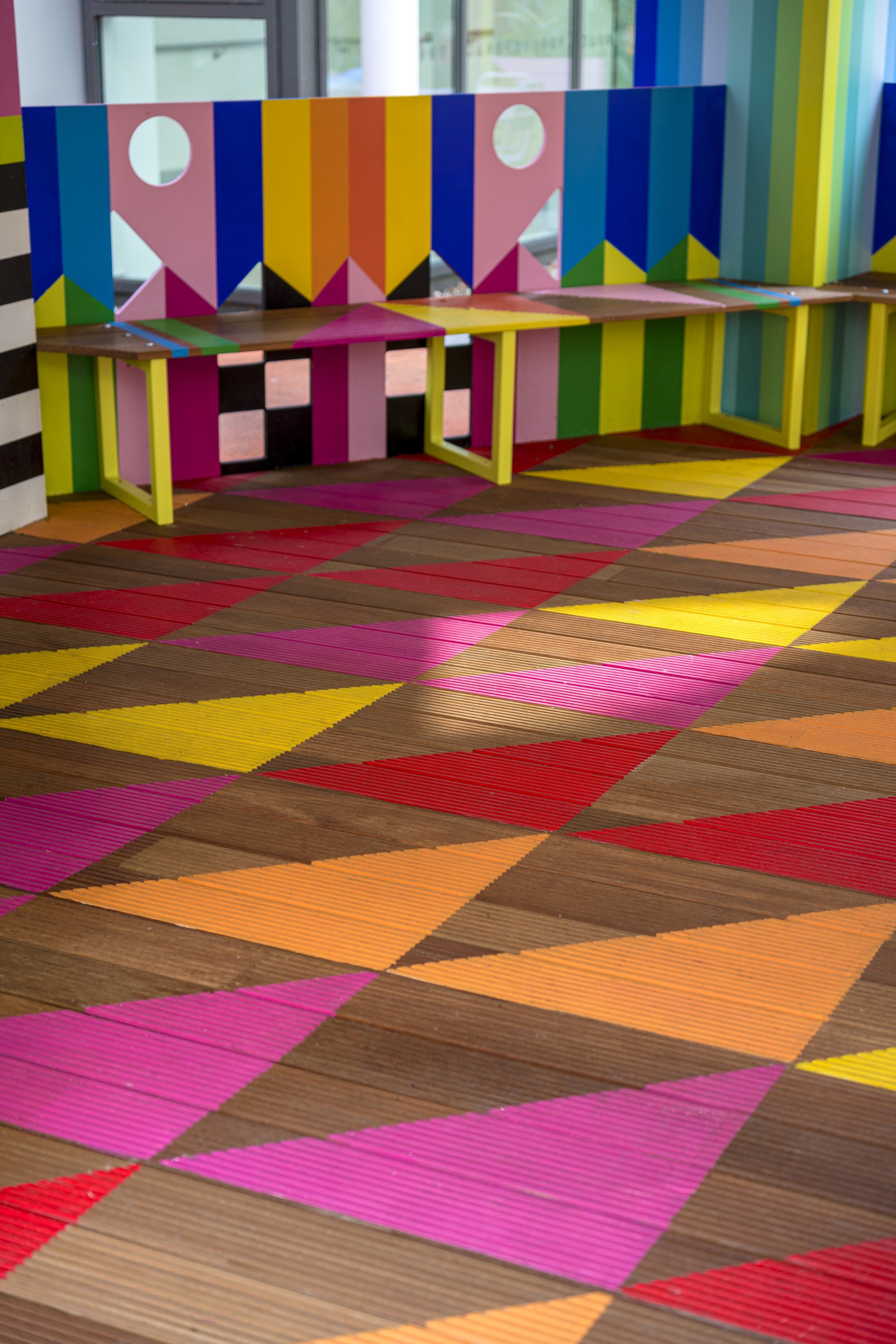 Interior timber decking with diagonal multicolored planks and benches against striped painted walls