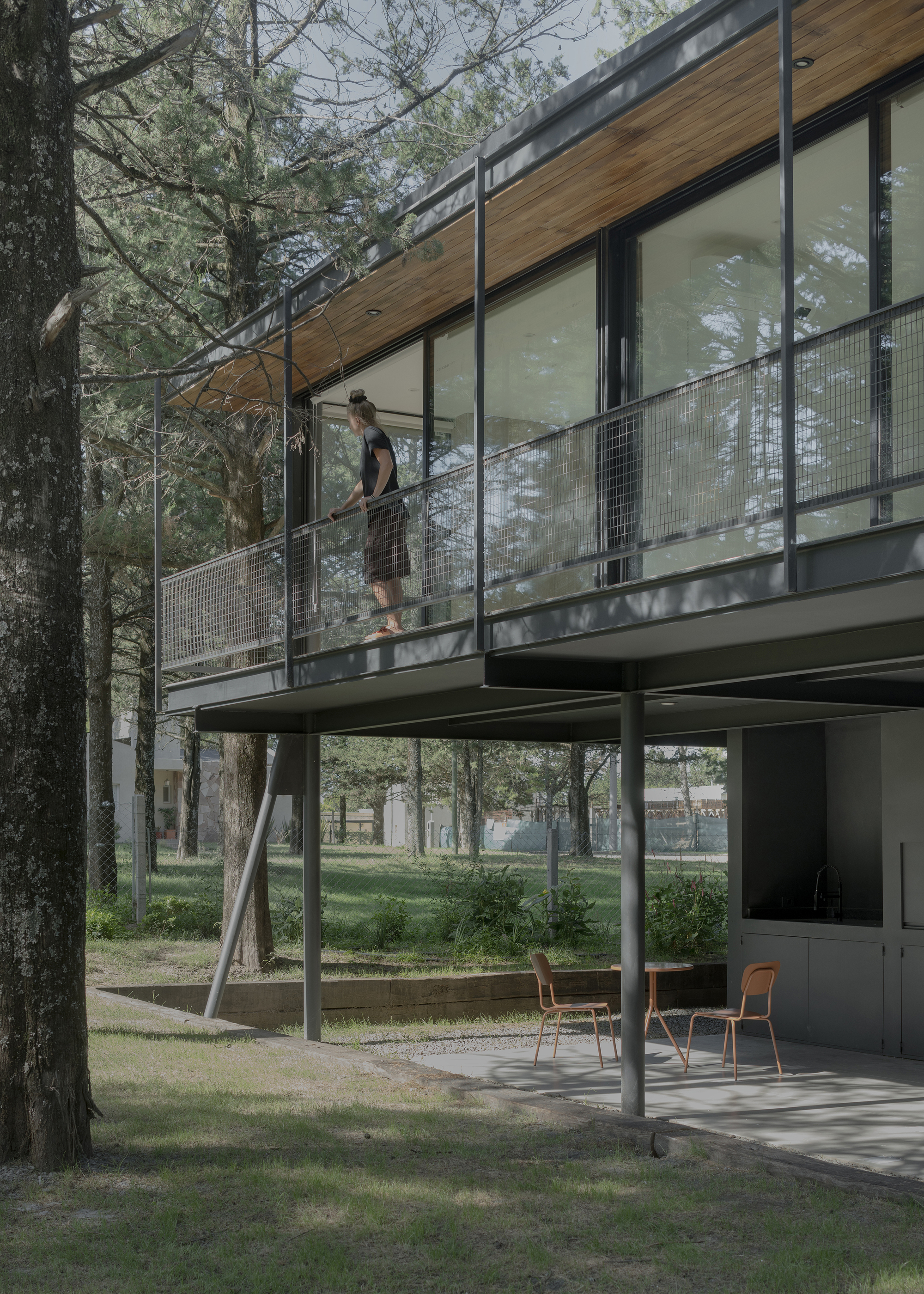 Figure descending exterior staircase with wire mesh railing beneath timber soffit and glass walls