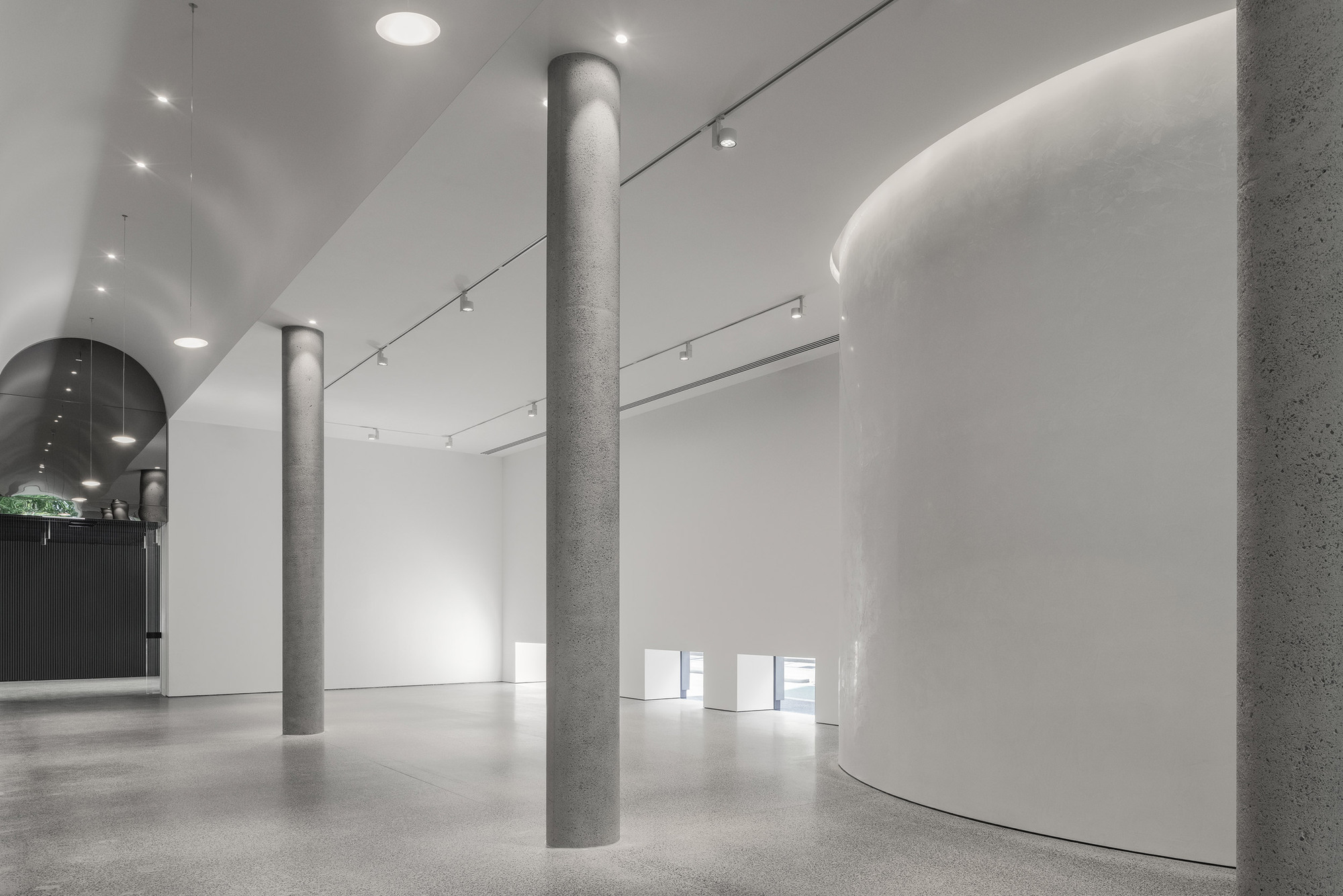White gallery interior with cylindrical concrete columns and curved walls beneath vaulted ceiling