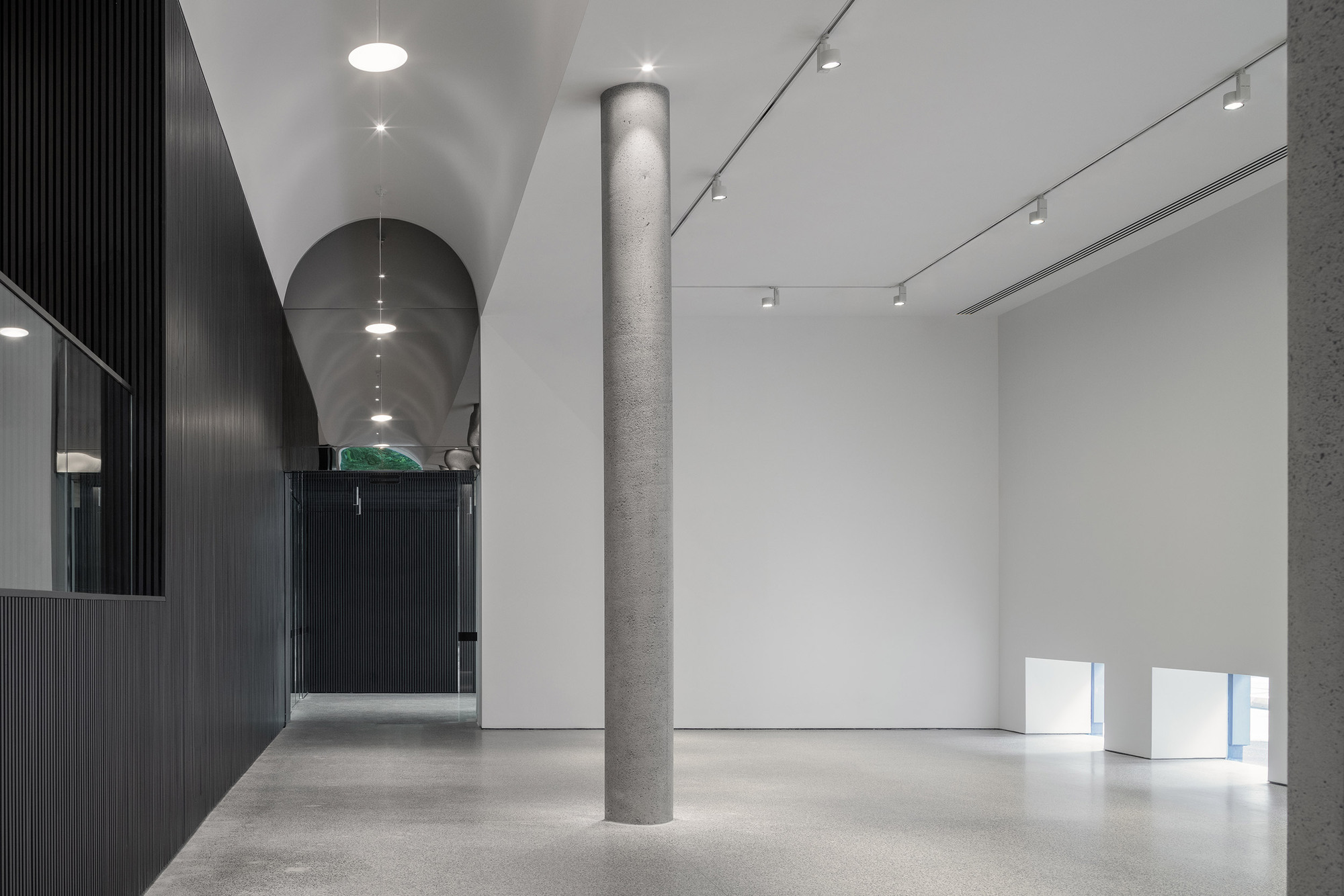 Gallery room with polished concrete floor, cylindrical grey column and low rectangular openings in white wall