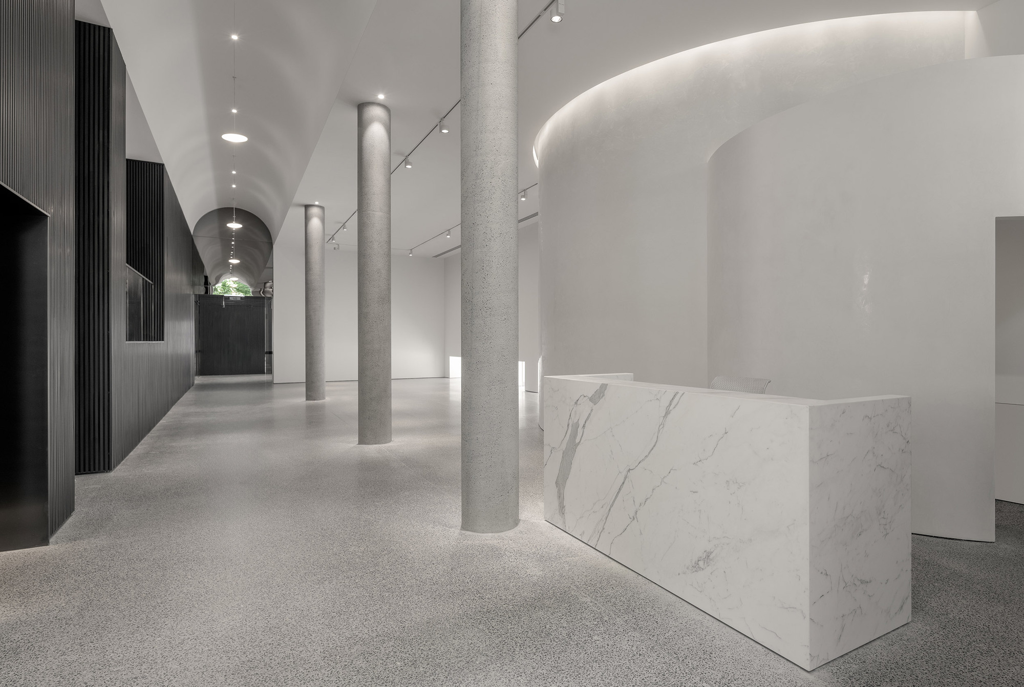 Corridor view with terrazzo columns flanking a marble reception counter and arched ceiling lit from above