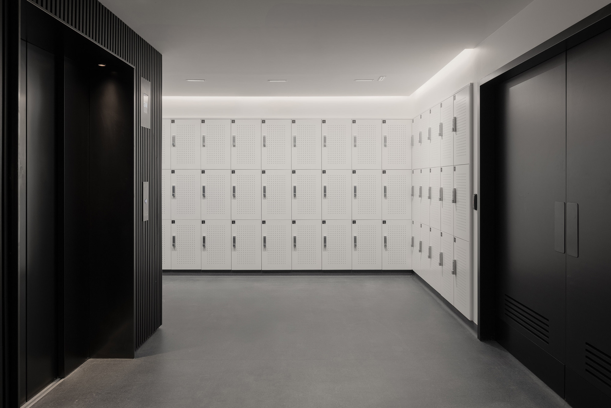 Locker room with white perforated metal lockers flanked by dark fluted wall panels and black storage units