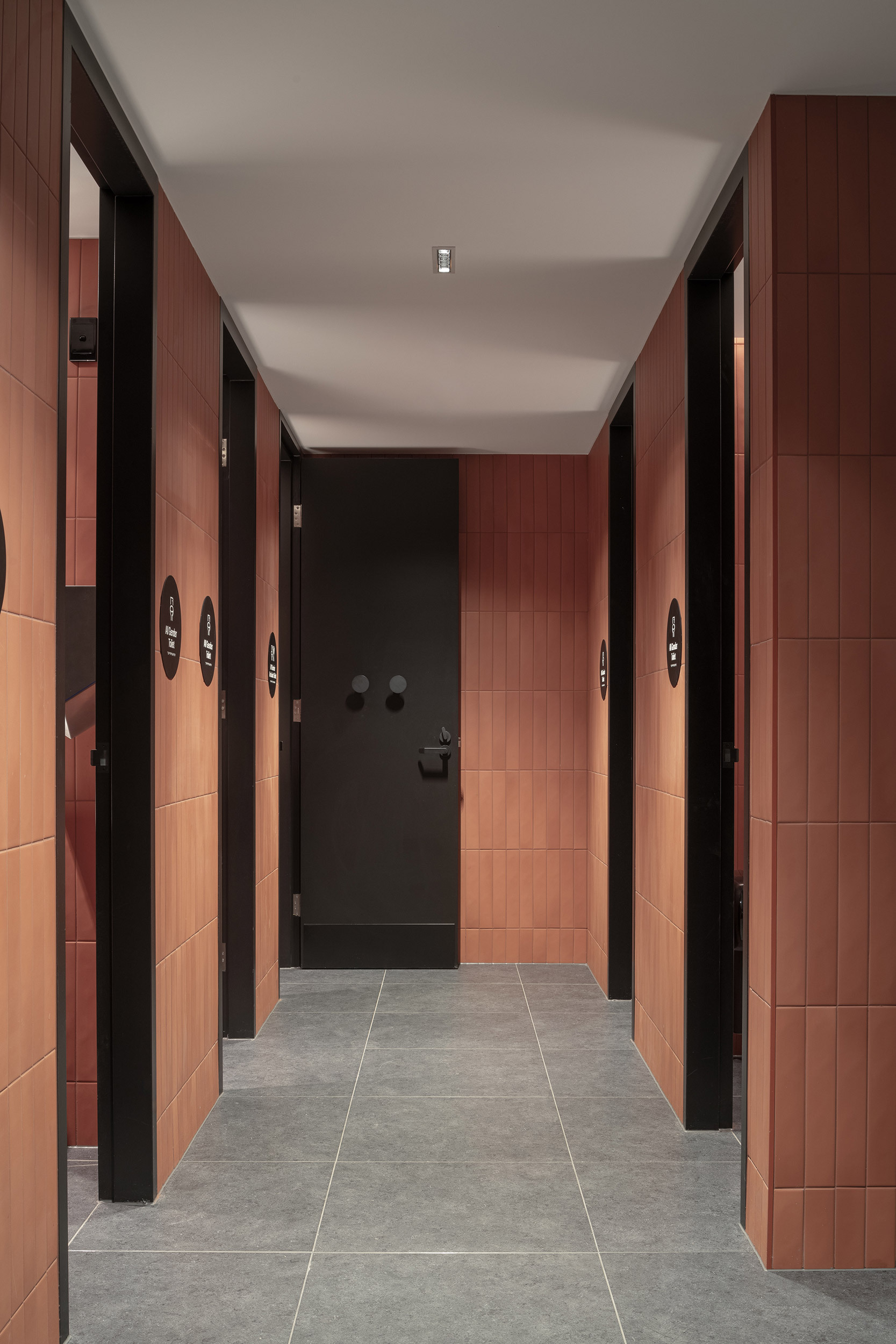 Corridor with terracotta tile walls, black-framed doors and grey stone flooring leading to a dark entry door