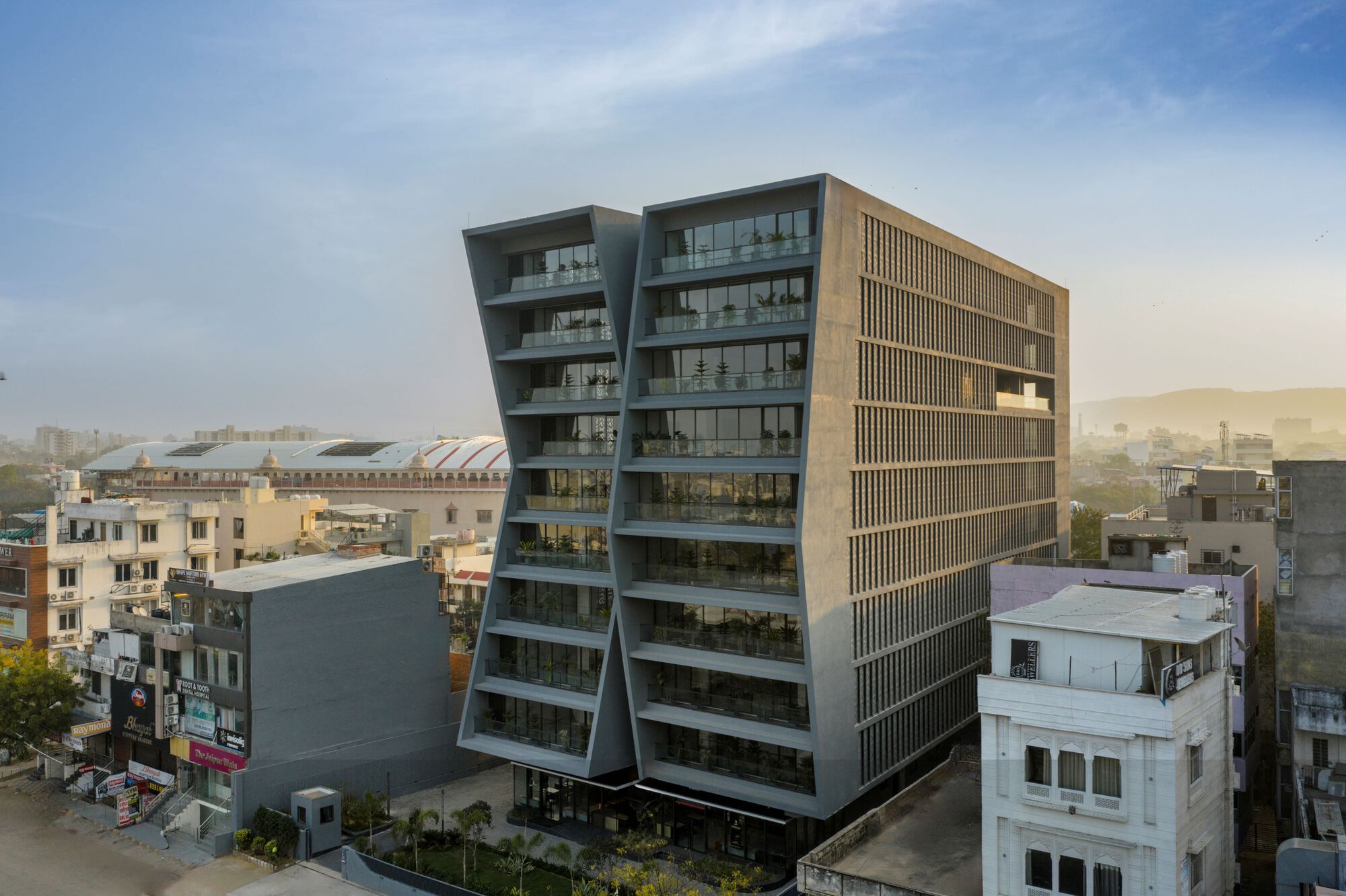 Aerial view of the angled glass and concrete tower rising above low-rise urban fabric in hazy afternoon light