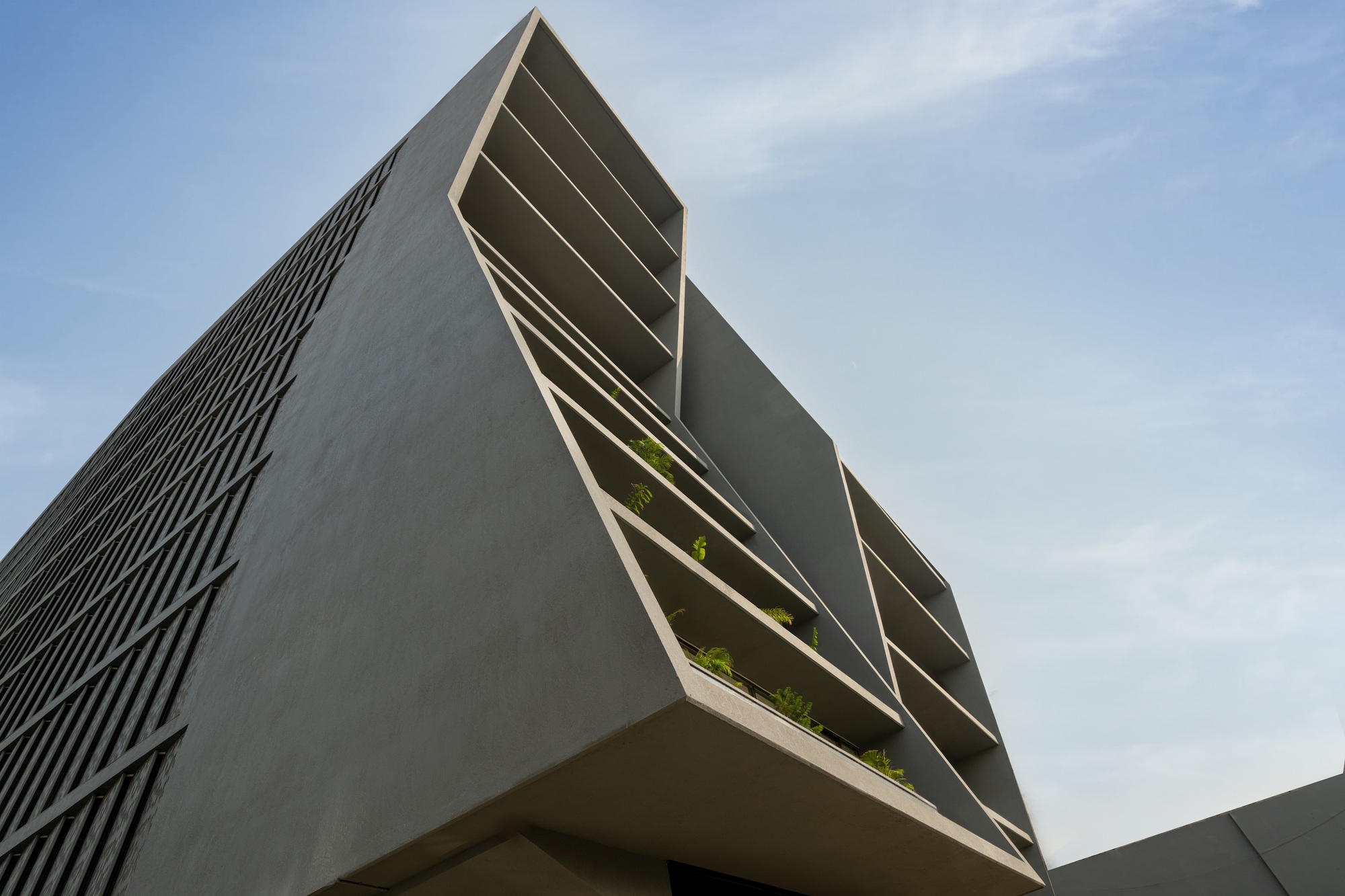 Corner detail of the cantilevered upper volume showing deep balcony recesses with planted troughs
