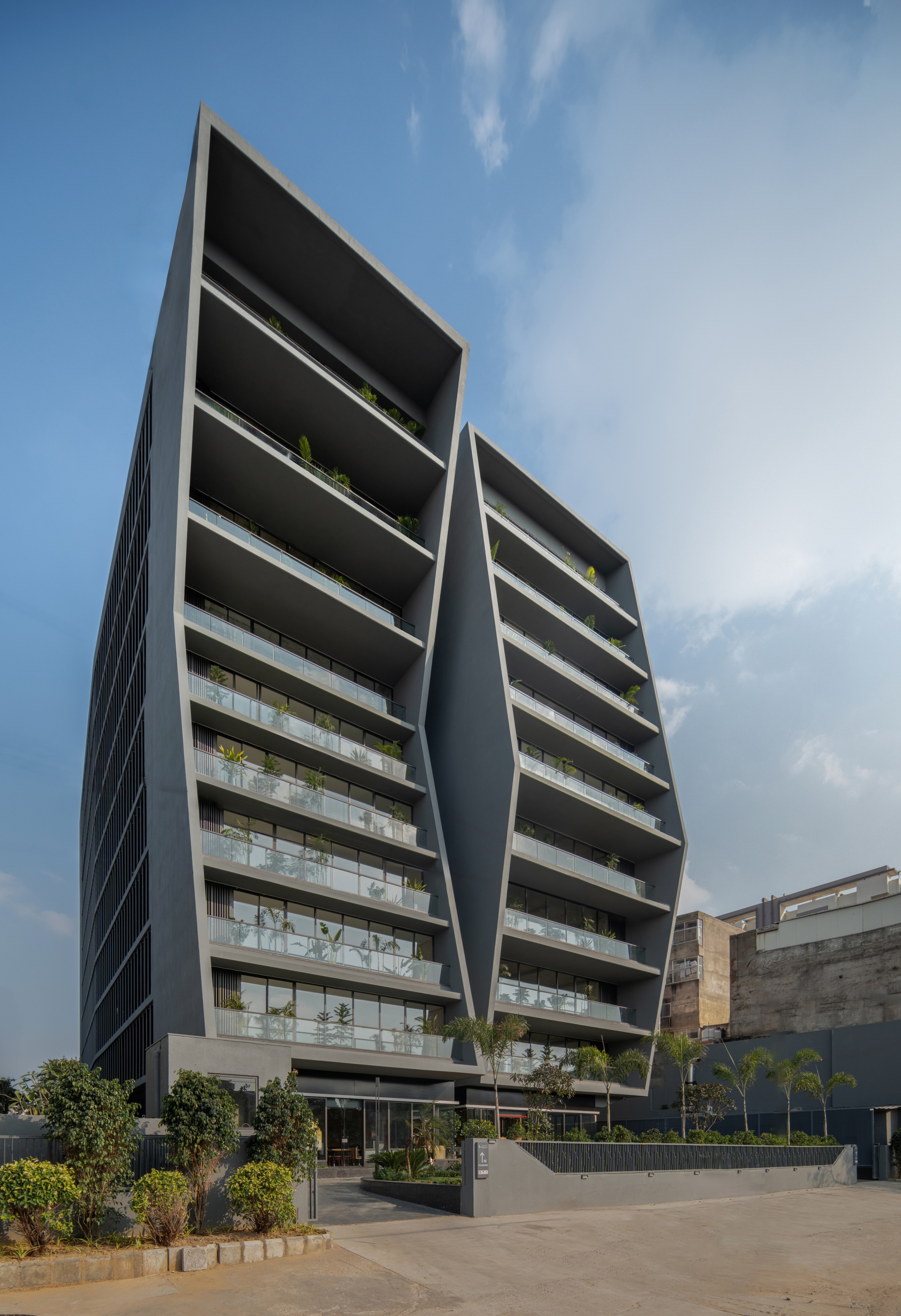 Full facade showing the paired towers with stepped balconies, ground-level planted beds and open plaza