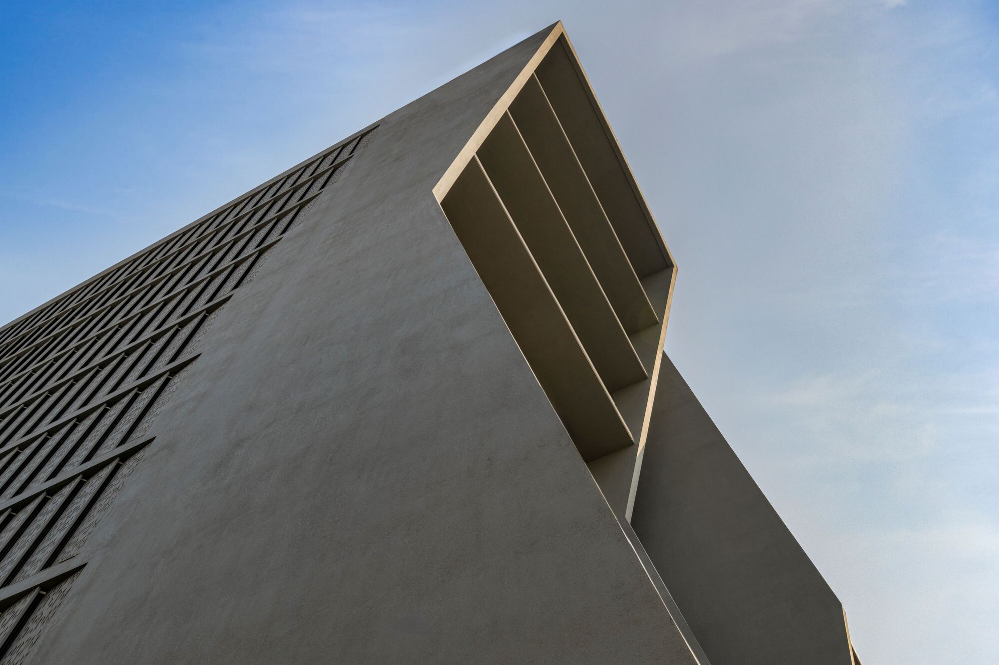 Upward view of the angular concrete tower with cantilevered louvered projection against a blue sky
