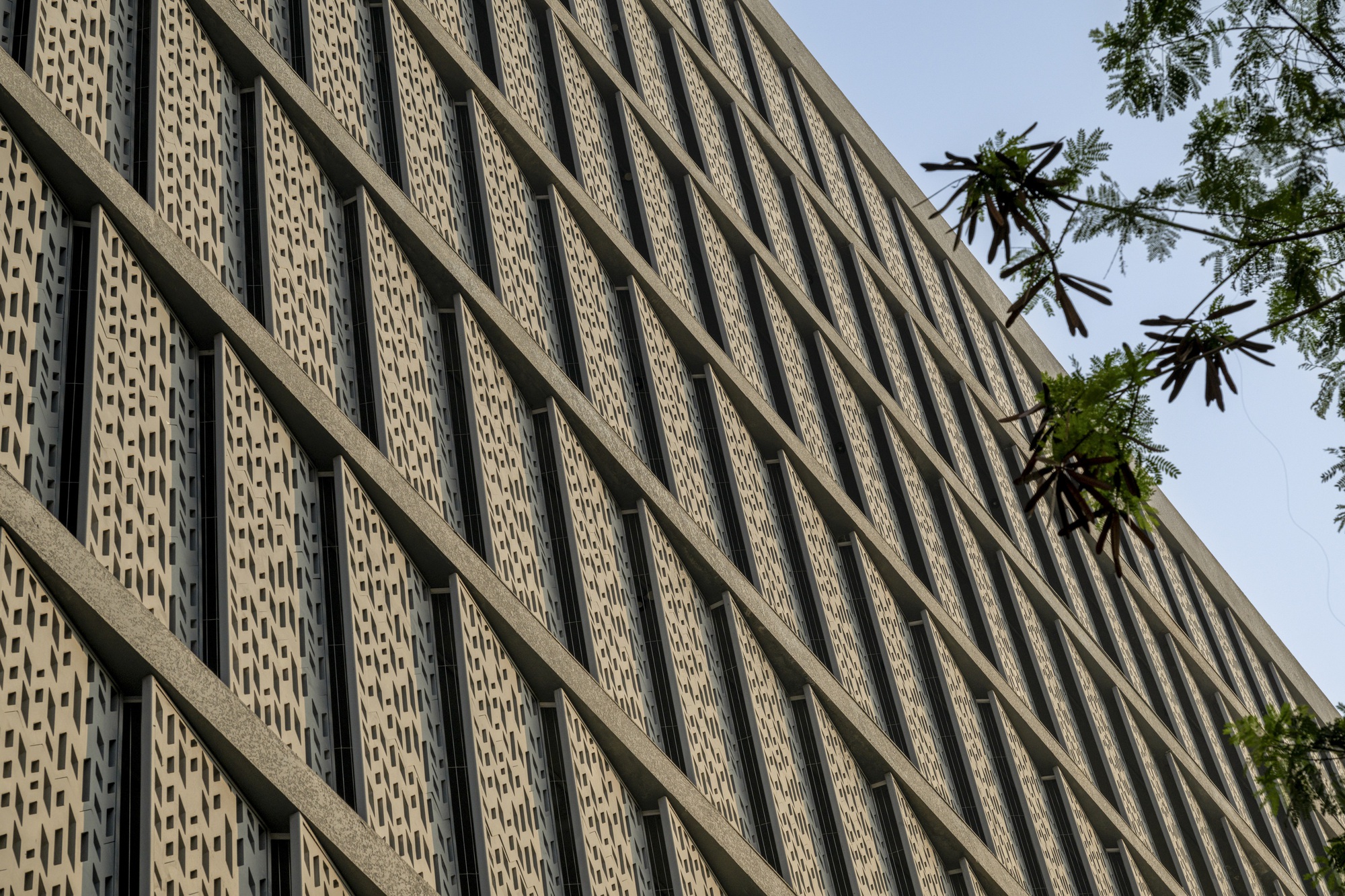 Diagonal view of the patterned brick screen wall with concrete grid framing beneath foliage