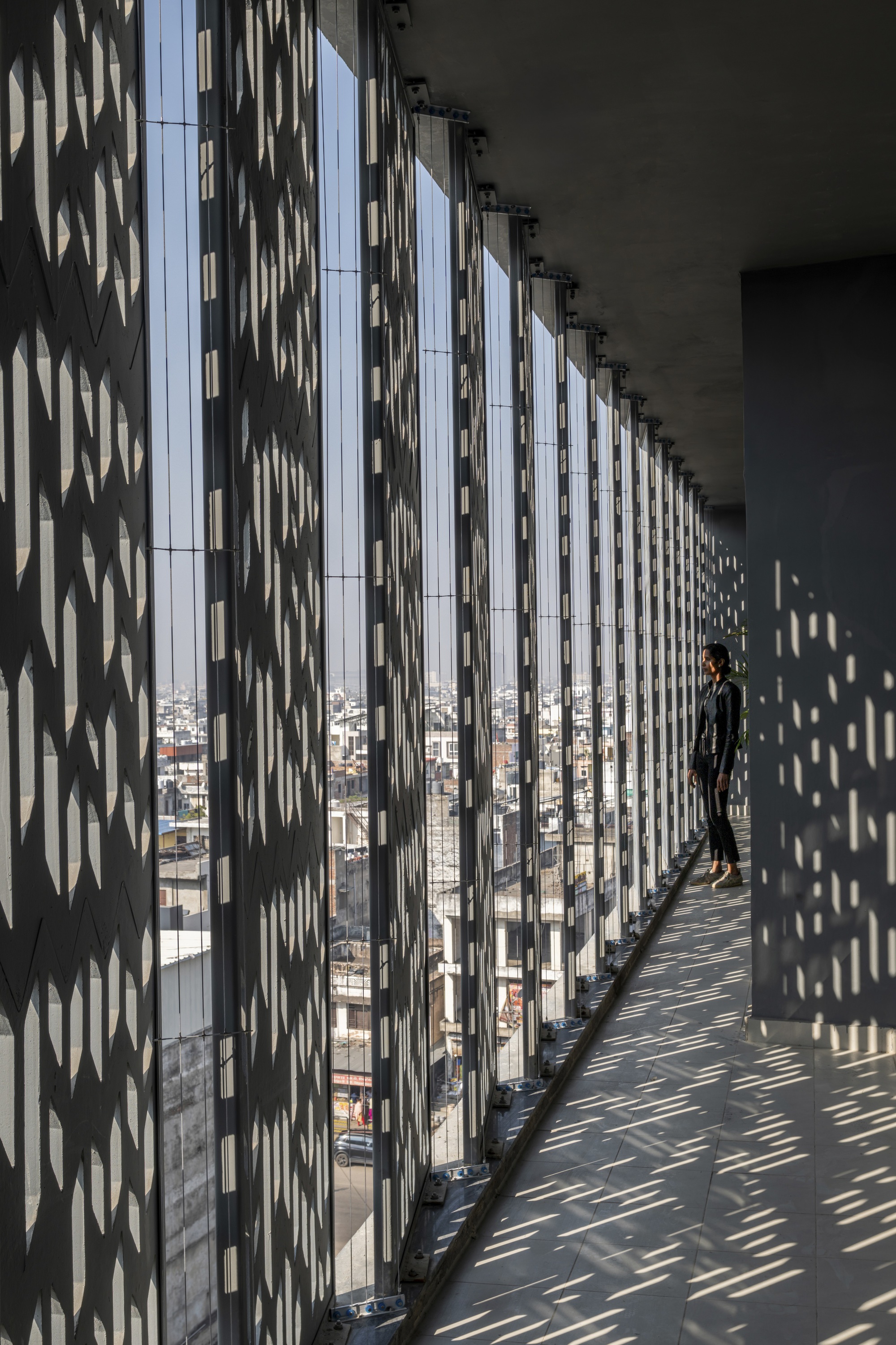 Perforated metal screen casting diagonal shadow patterns on the corridor floor with a figure visible
