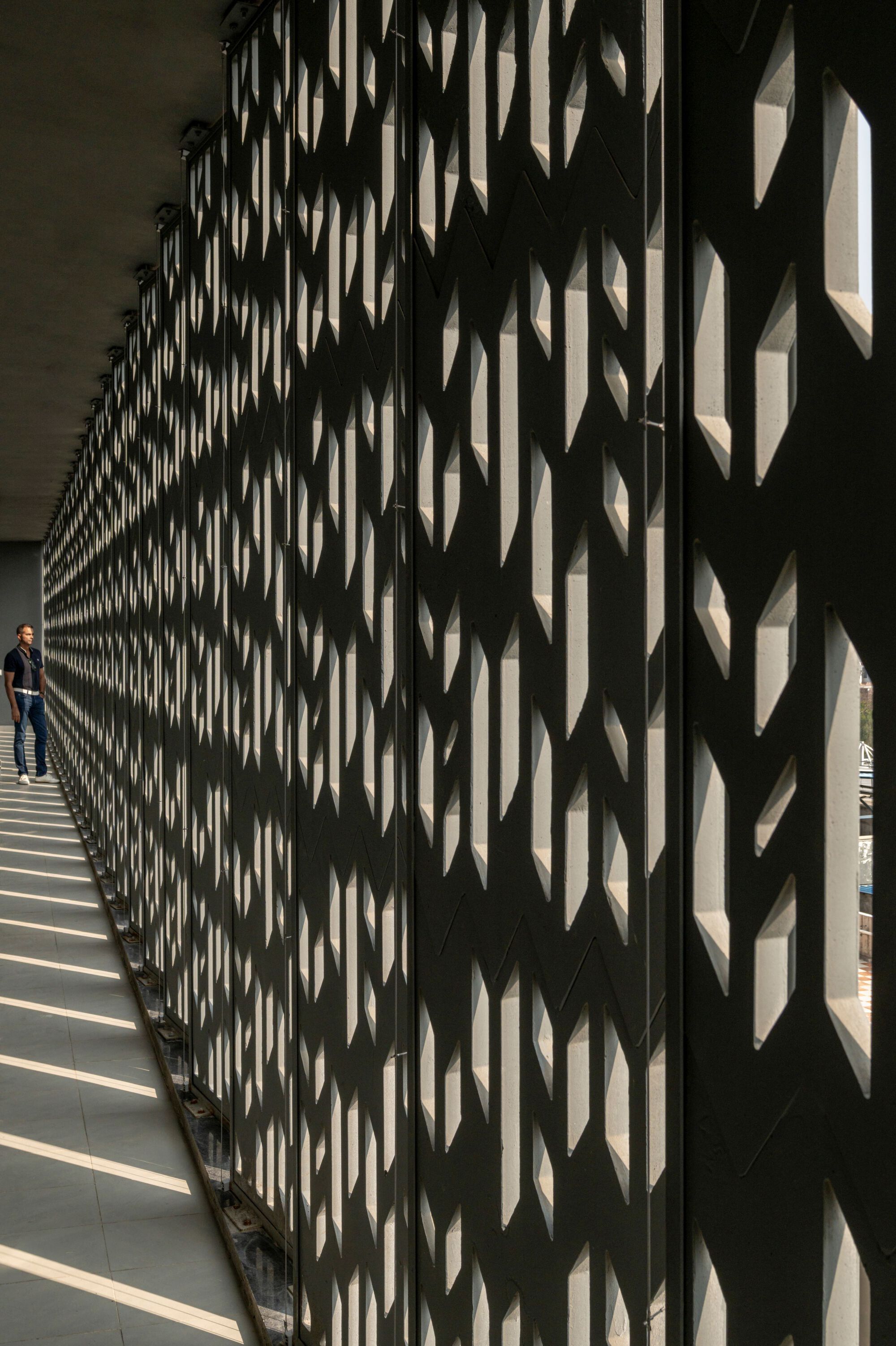 Chevron-patterned screen wall creating layered shadows along the interior walkway with a person standing